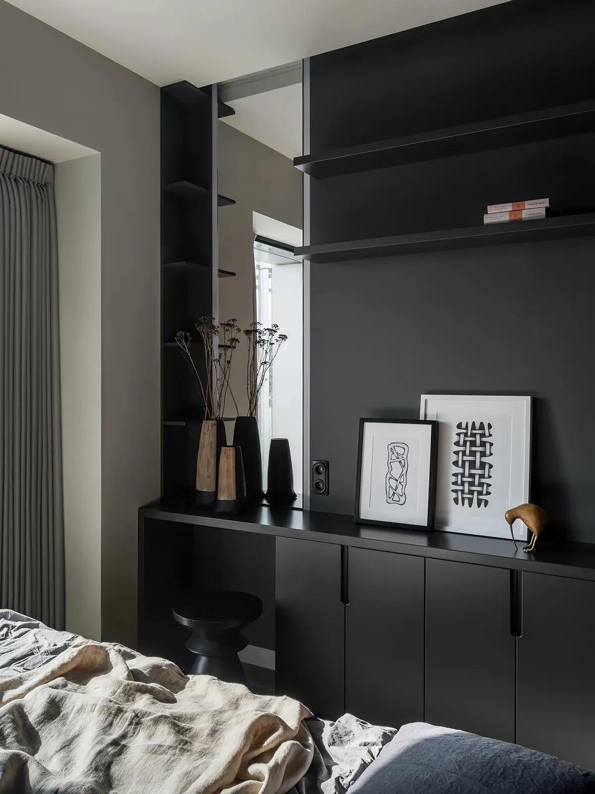 Угол спальни в темных тонах с черными полками, вазами с сухоцветами, абстрактными картинами