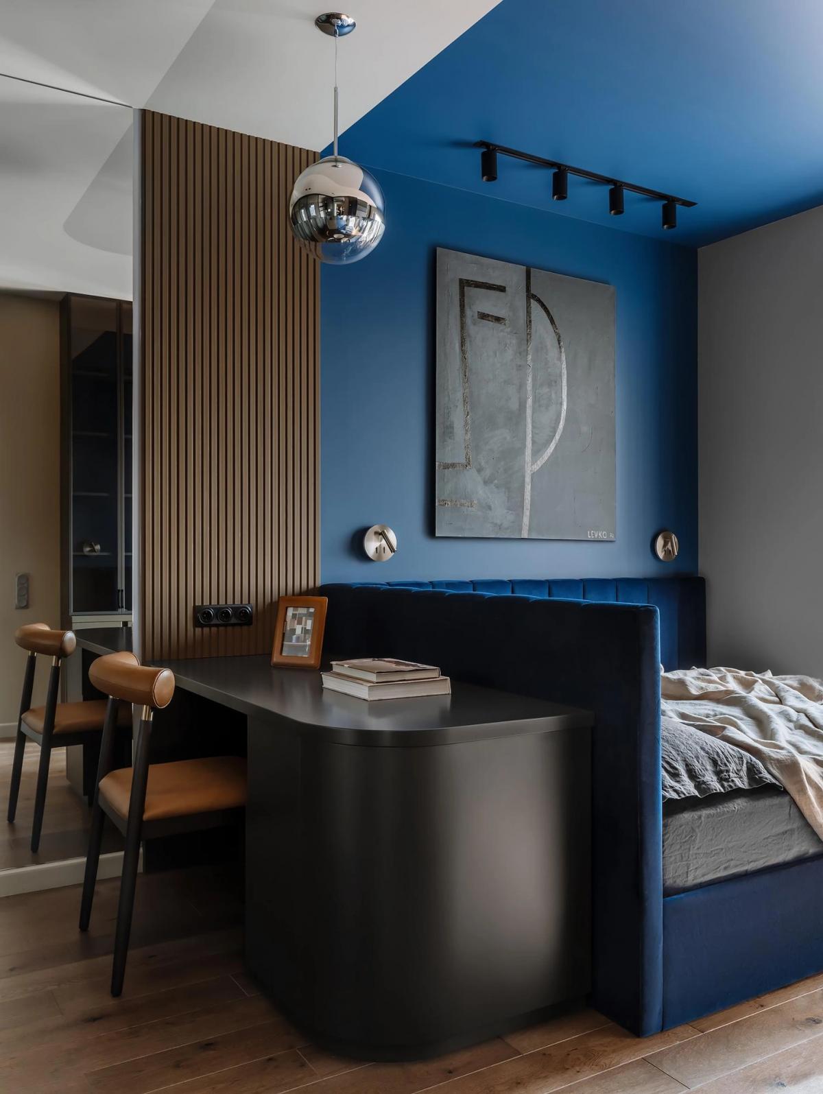 Спальня с синей стеной и потолком, деревянными рейками, черным рабочим столом