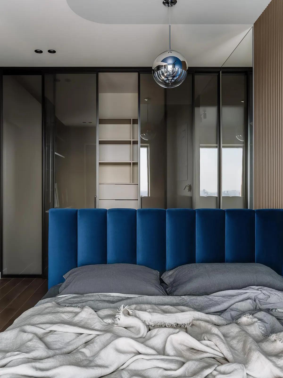 Кровать с синим бархатным изголовьем и серыми подушками