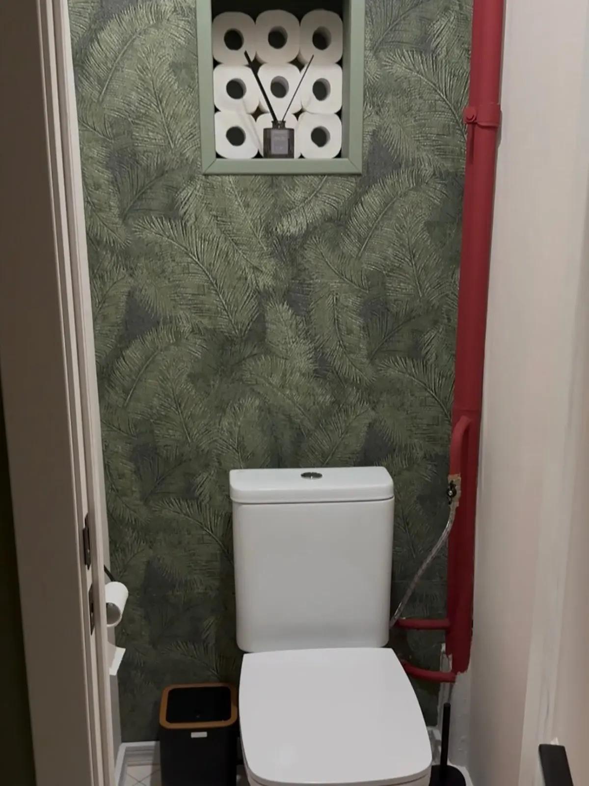 Туалет с тропическими обоями, туалетной бумагой в нише, диффузором и красной трубой