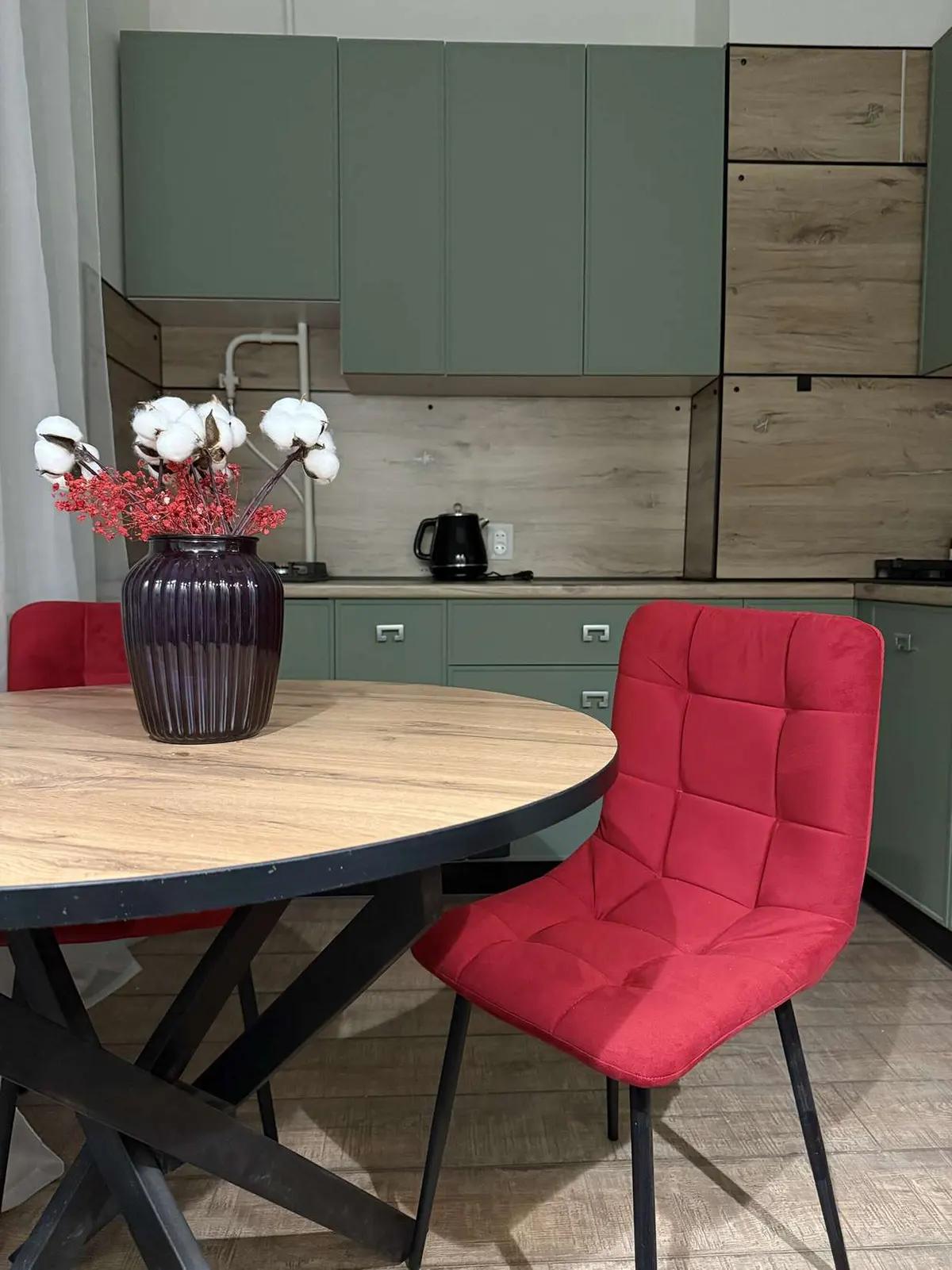 Кухня: круглый деревянный стол, красный стул, ваза с хлопком и шкафы мятного цвета