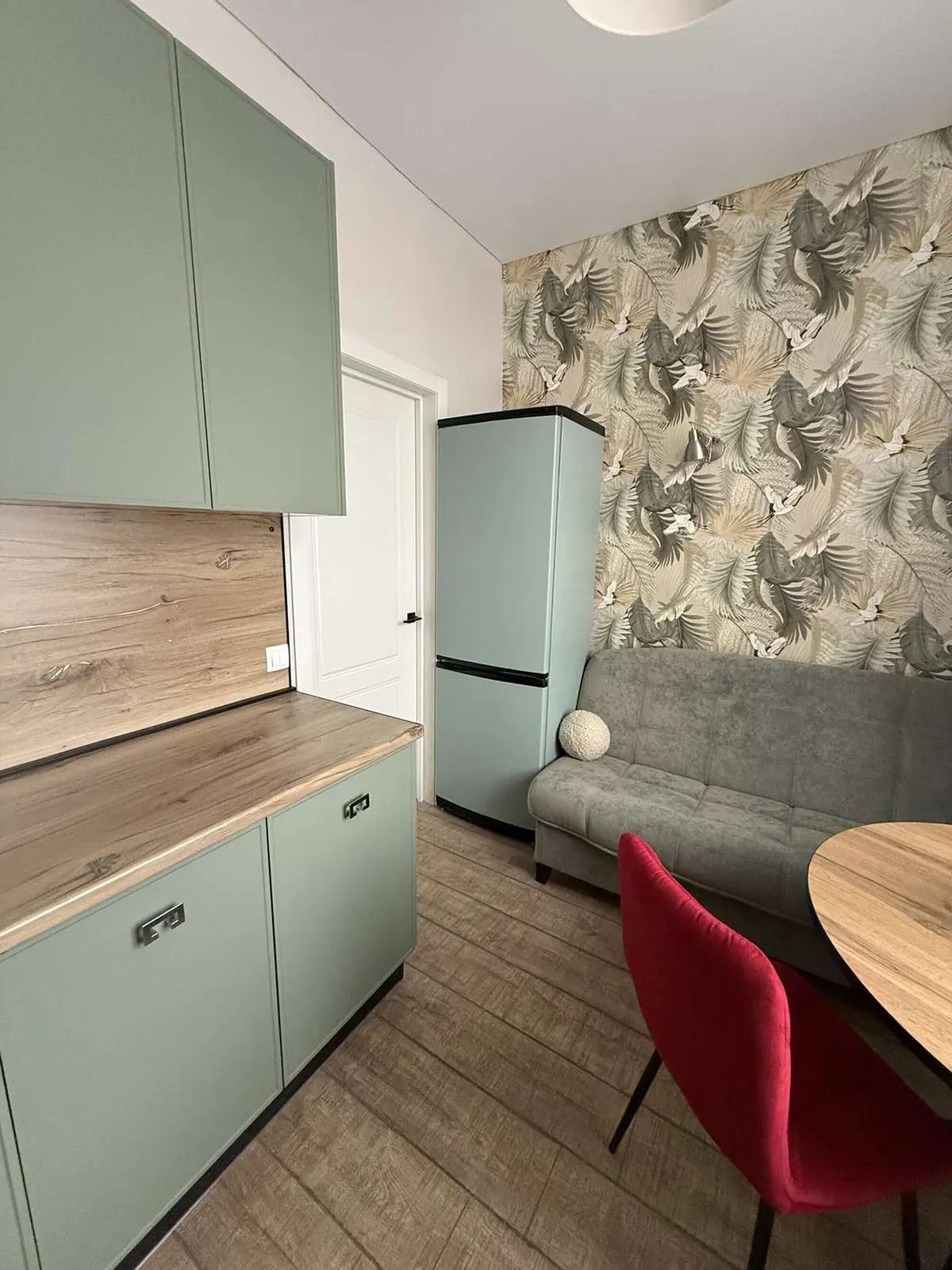 Кухня с мятным холодильником, серым диваном, красным стулом и круглым деревянным столом 