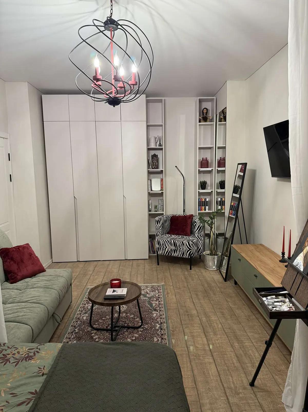 Гостиная с кроватью, диваном, креслом, полками, ТВ на стене и мольбертом