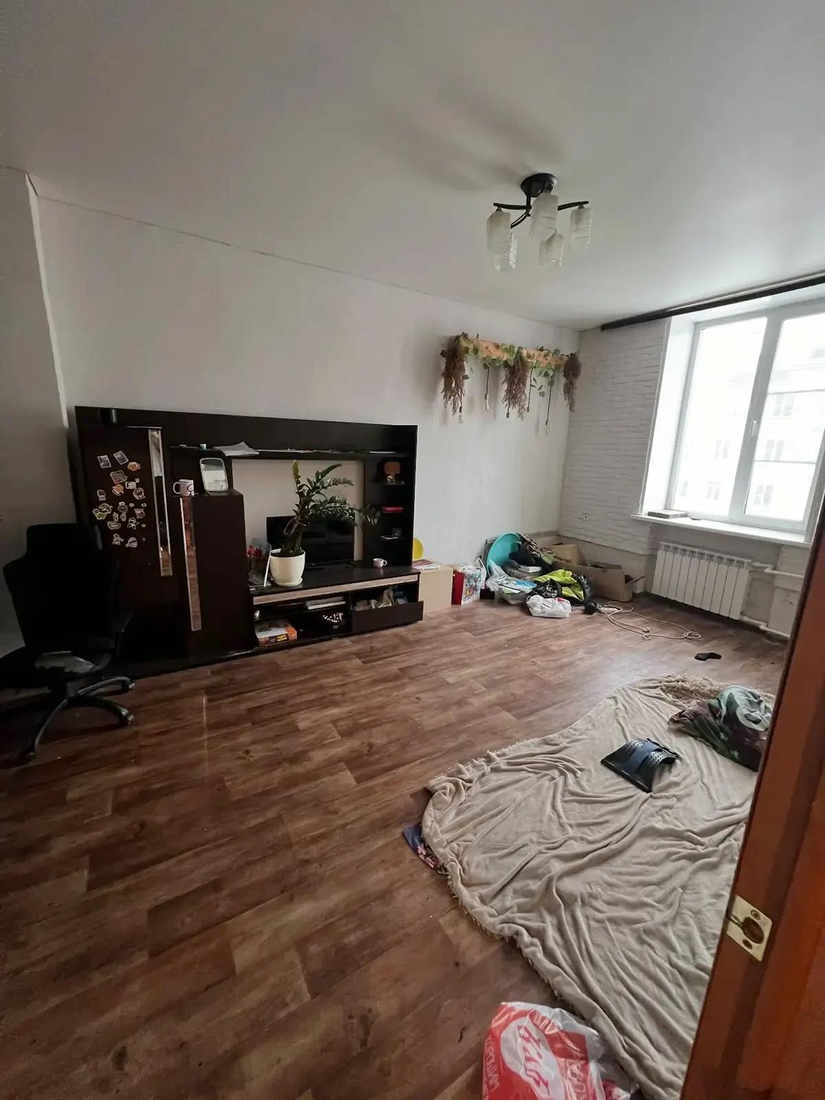 Захламленная гостиная с тумбой под ТВ, стулом и вещами на полу до ремонта