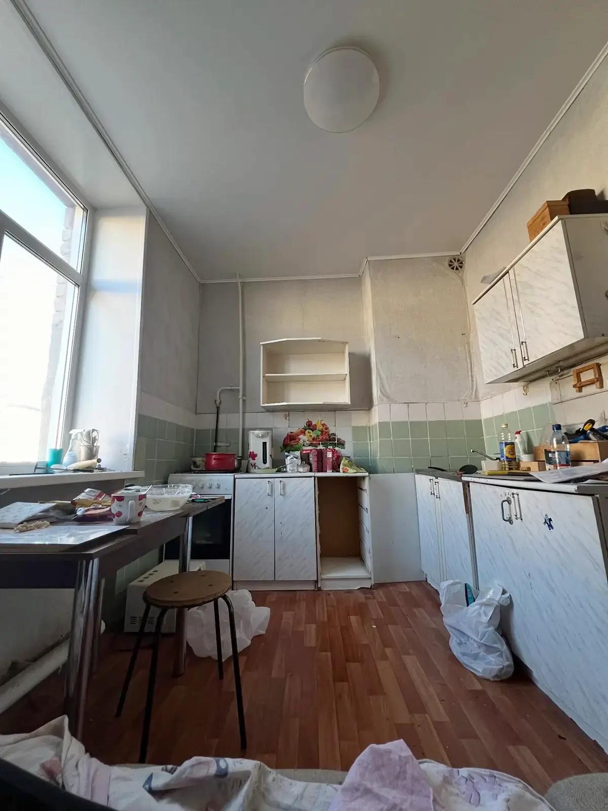 Кухня до ремонта со старым кухонным гарнитуром, столом, посудой и белыми пакетами на полу