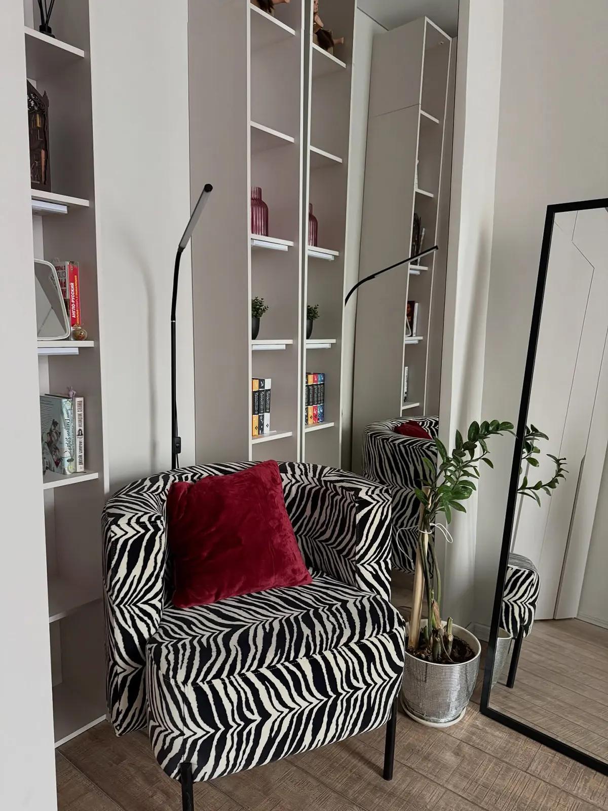 Кресло с зебровым узором, красной подушкой на фоне книжного шкафа в гостиной