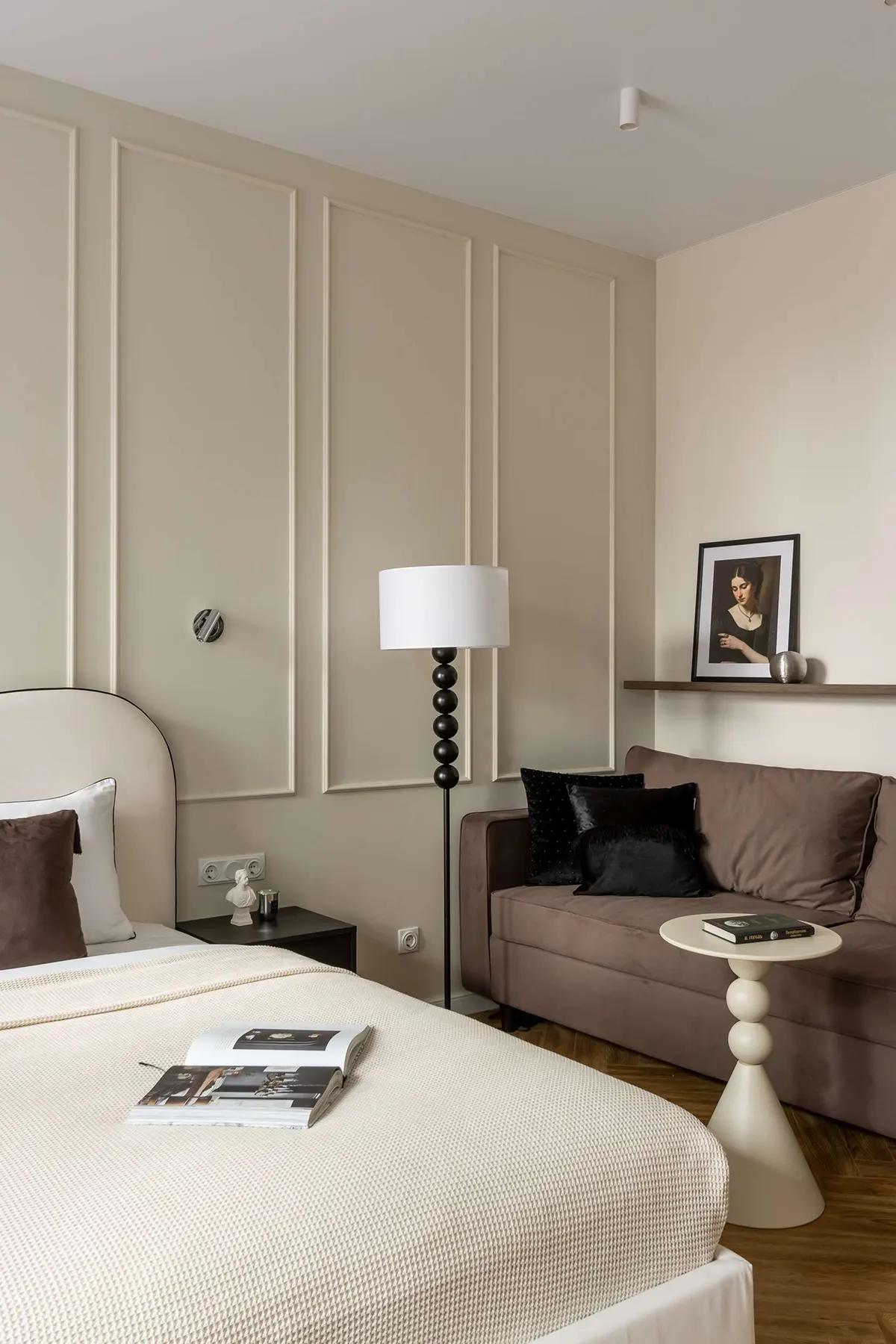 Элегантный уголок в квартире-студии с коричневым диваном, напольной лампой, картиной на полке