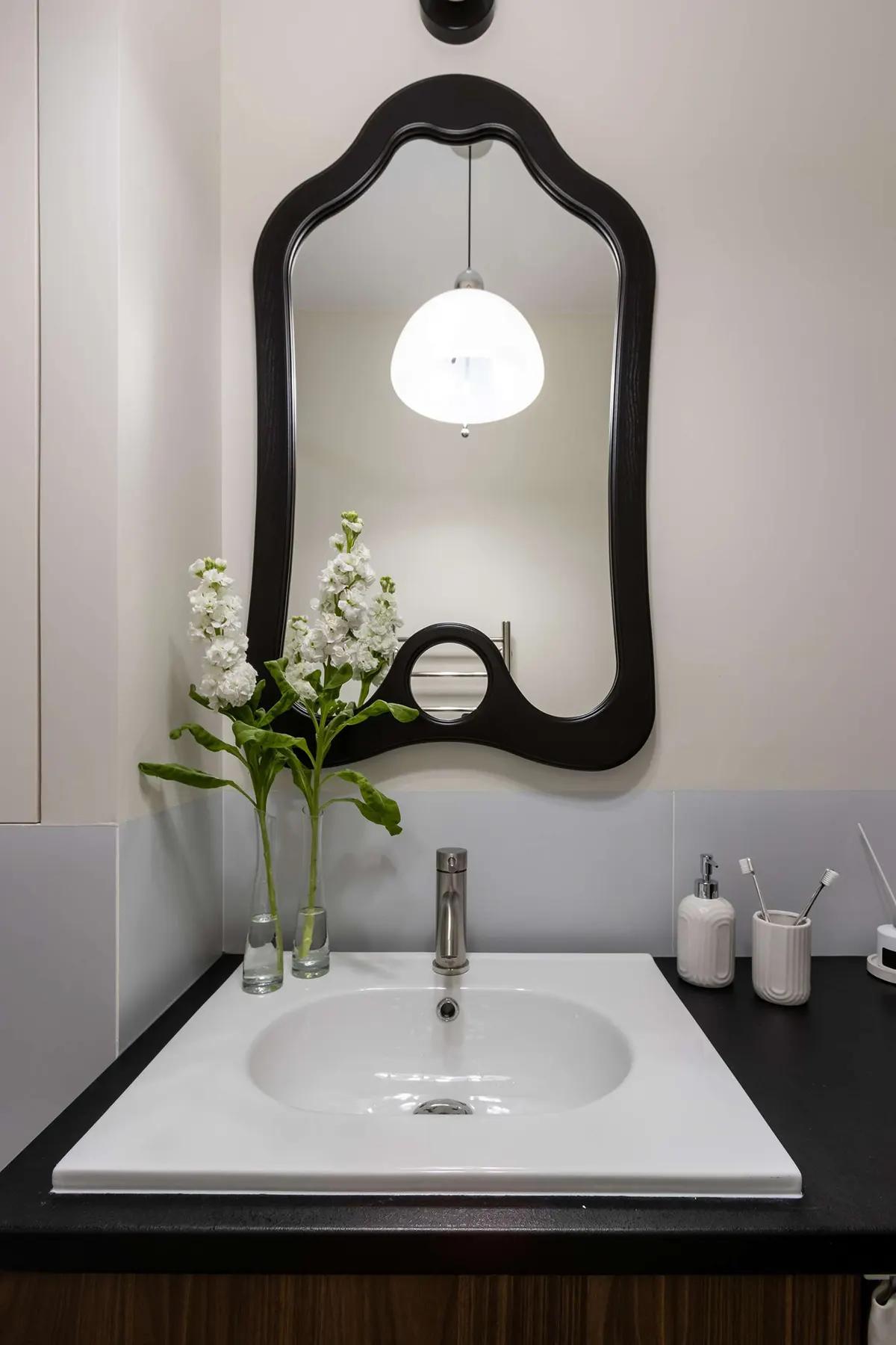Стильный умывальник в ванной комнате с черным фигурным зеркалом