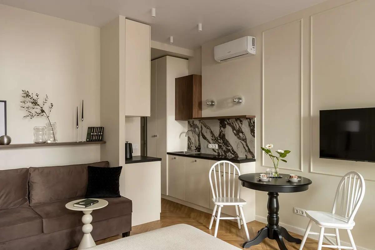 Вид на обеденную зону в квартире-студии 30 кв.м. Черный круглый стол, белые стулья, коричневый диван