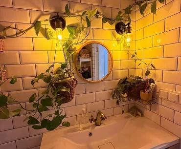 Уютный уголок в ванной комнате с раковиной, растениями, круглым зеркалом.