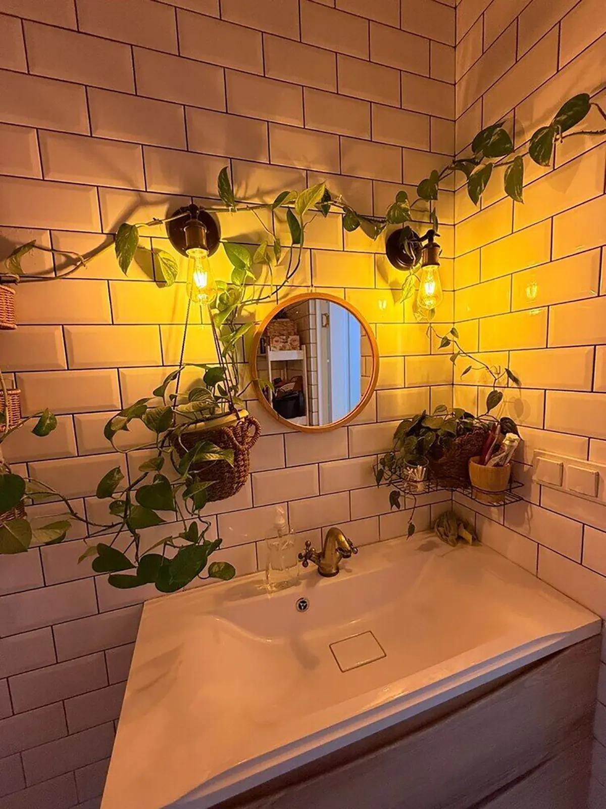 Уютный уголок в ванной комнате с раковиной, растениями, круглым зеркалом.