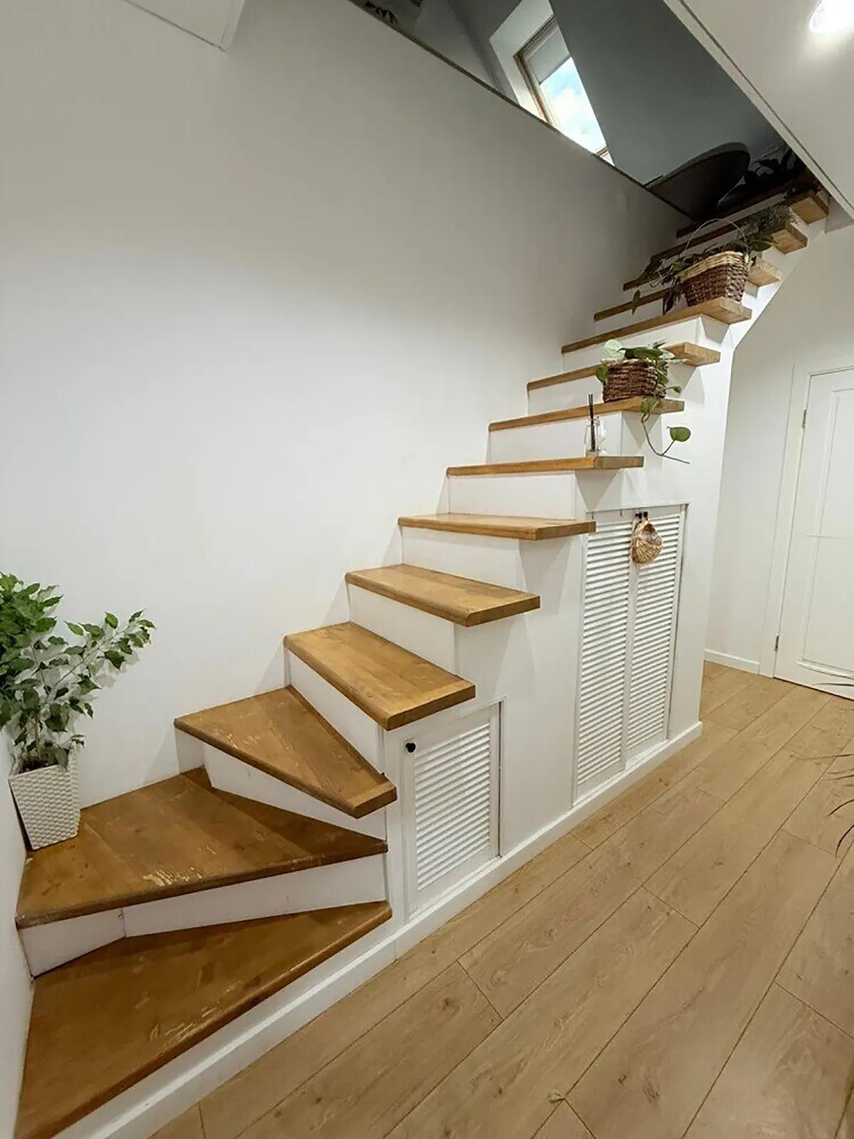 Деревянная лестница на мансарду с белыми перилами, растениями на ступенях и белыми шкафами