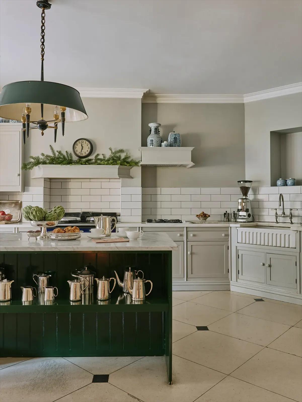 Кухня с тёмно-зелёным островом, мраморной столешницей, серебряными кувшинами, часами и еловыми ветками