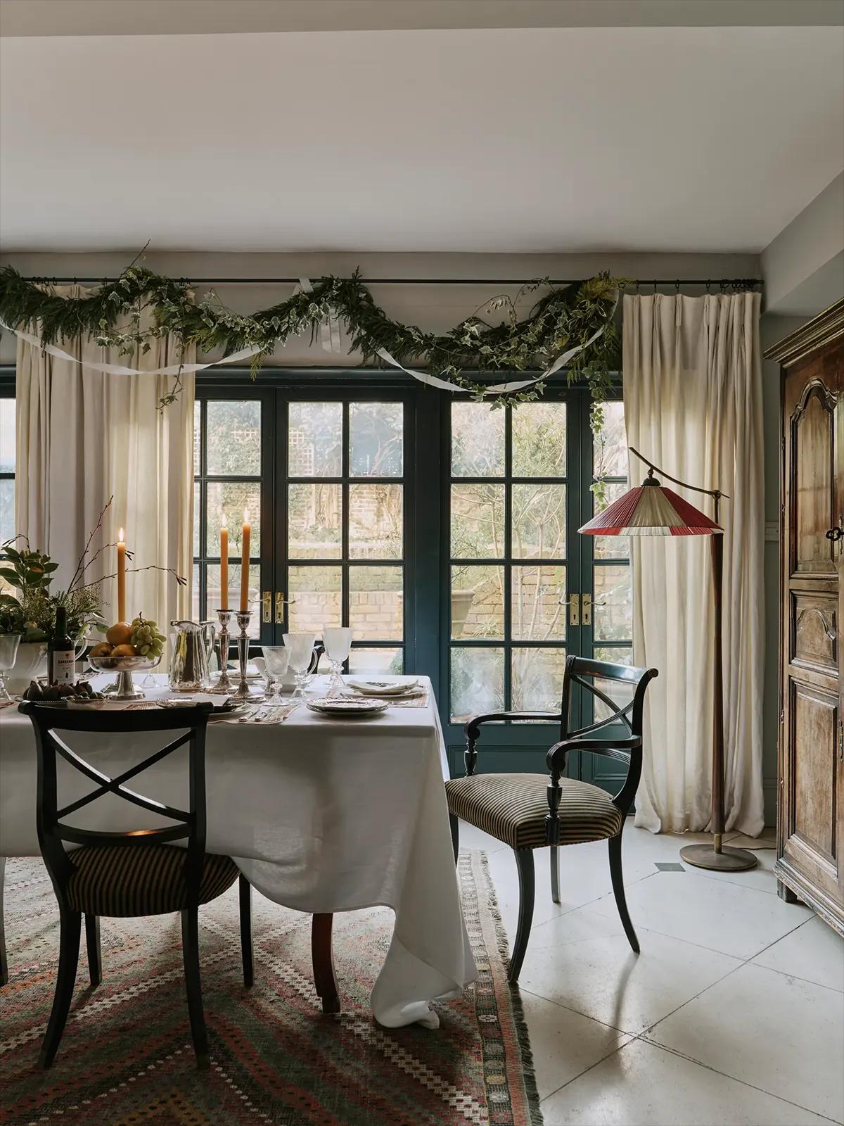 Обеденный стол с белой скатертью; рождественское украшение над окном