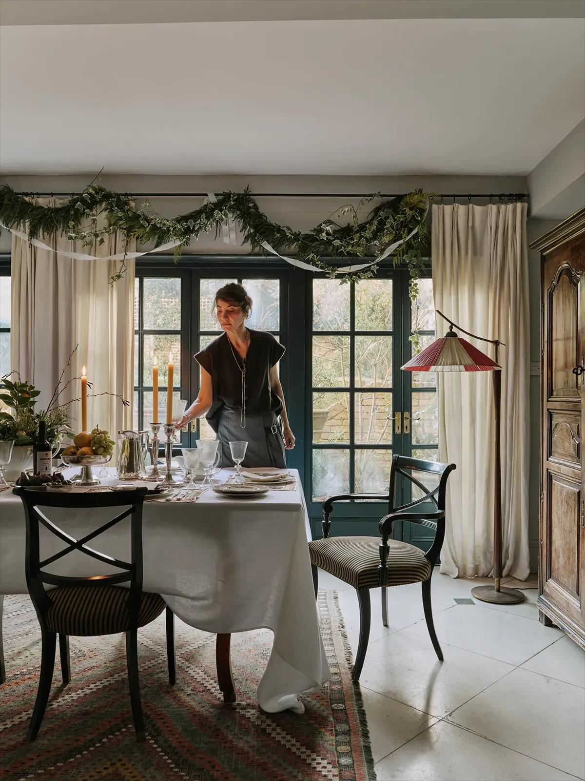 Женщина расставляет посуду на столе с белой скатертью