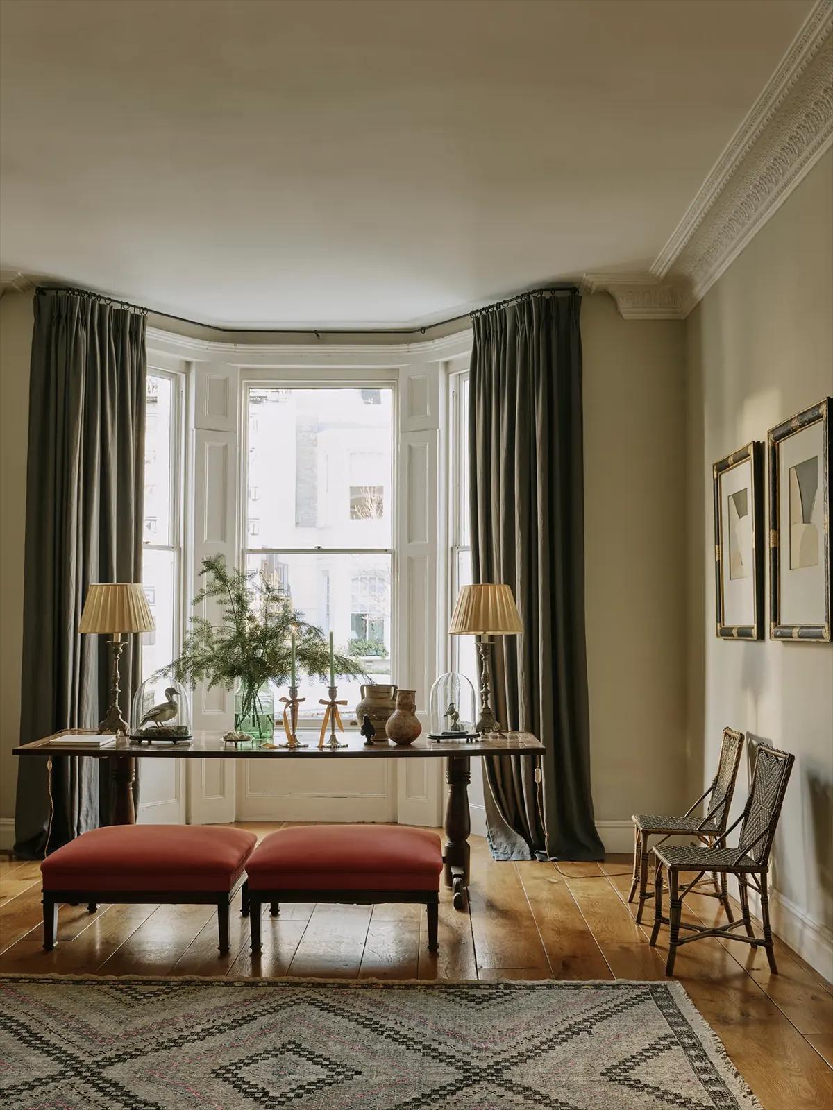 Деревянный стол у эркера со свечами, глиняными горшками, двумя настольными лампами и еловыми ветками в вазе