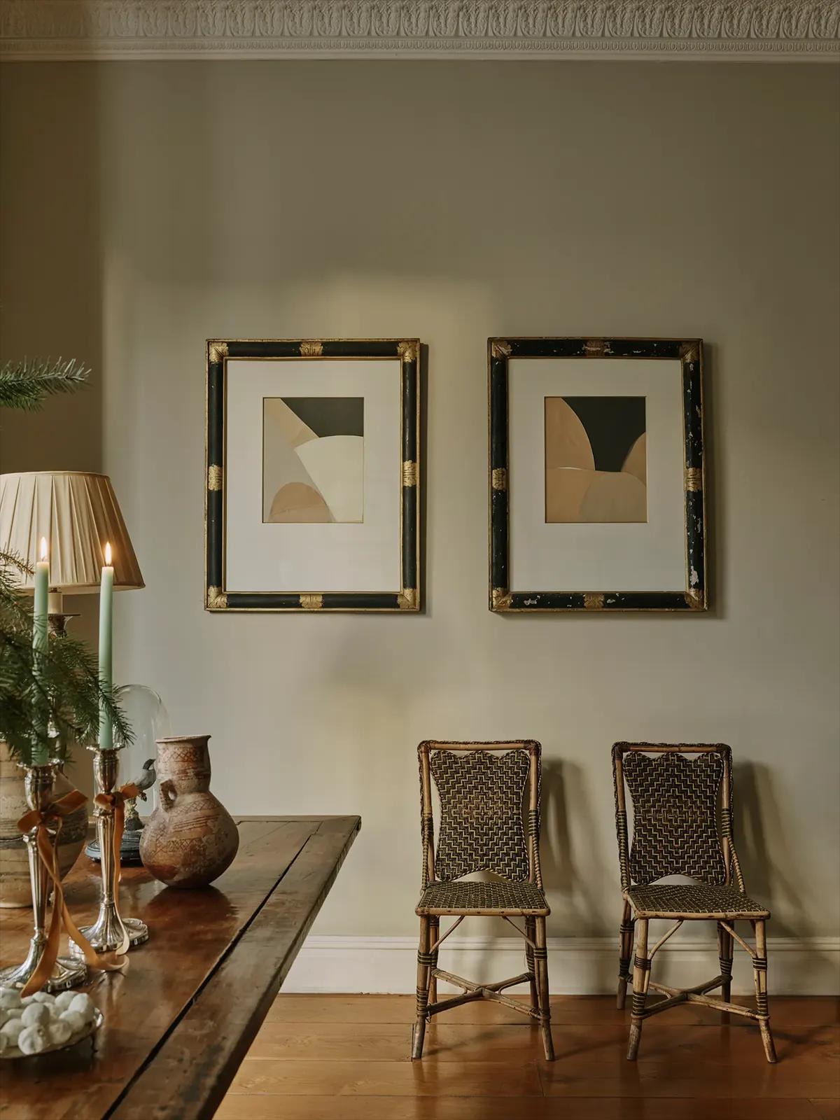 Деревянный стол с зелёными свечами, плетёными стульями, абстрактными картинами и рождественским декором