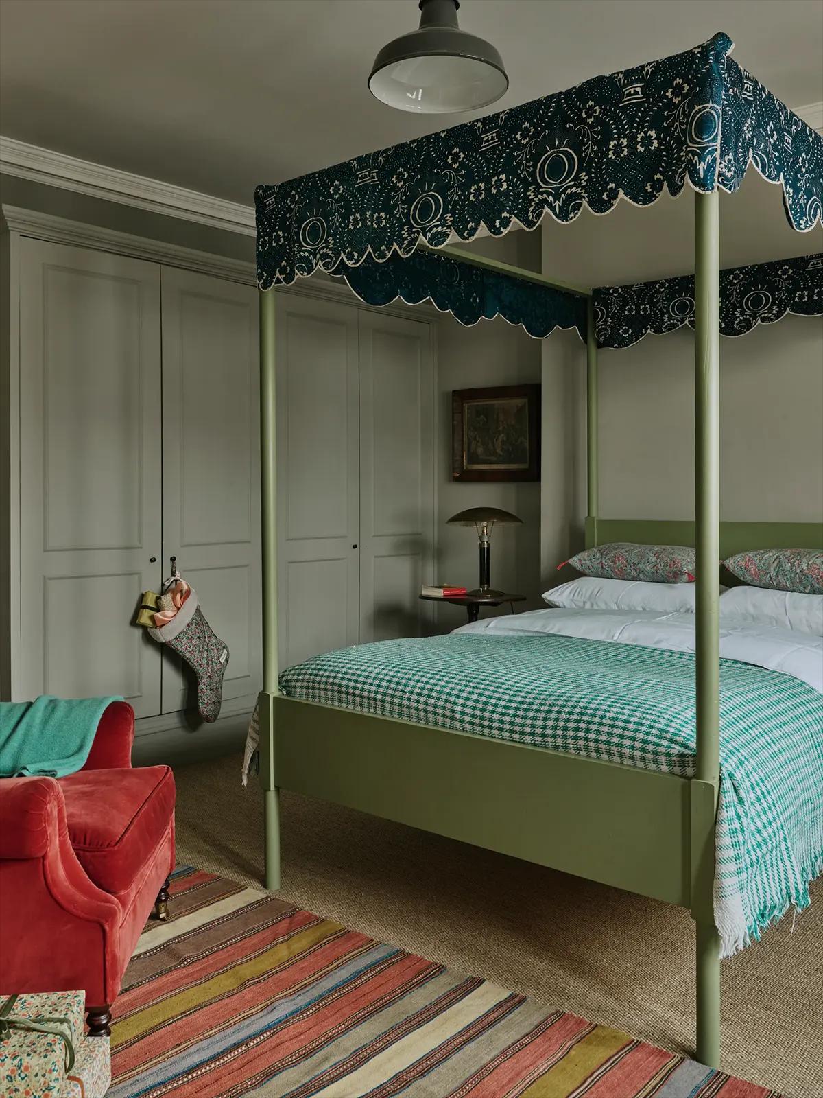 Спальня с зелёной кроватью-балдахином, клетчатым пледом, рождественским носком, красным креслом и узорчатым ковром