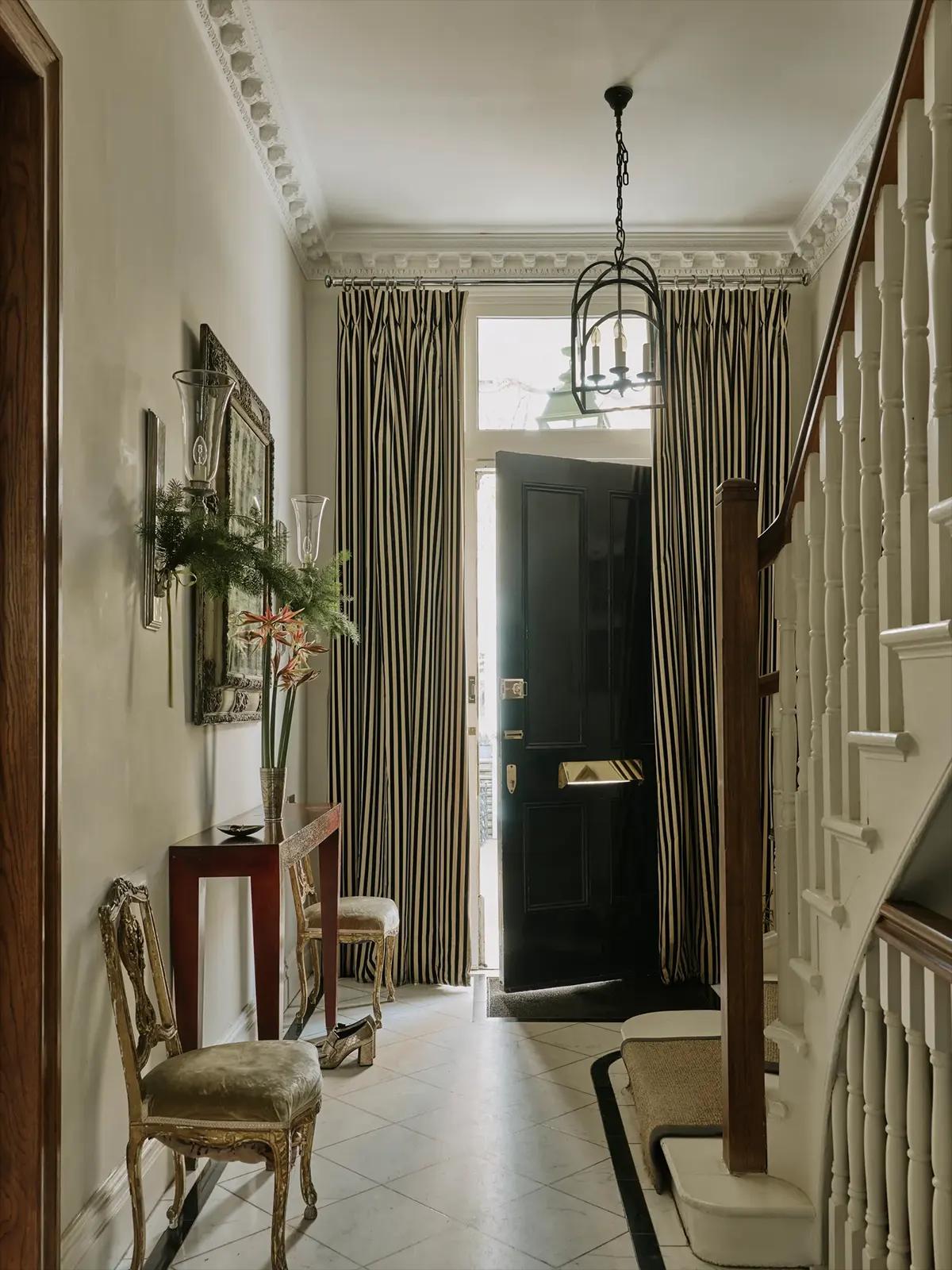 Прихожая с чёрной дверью, полосатыми шторами, консольным столико и позолоченными винтажными стульями 