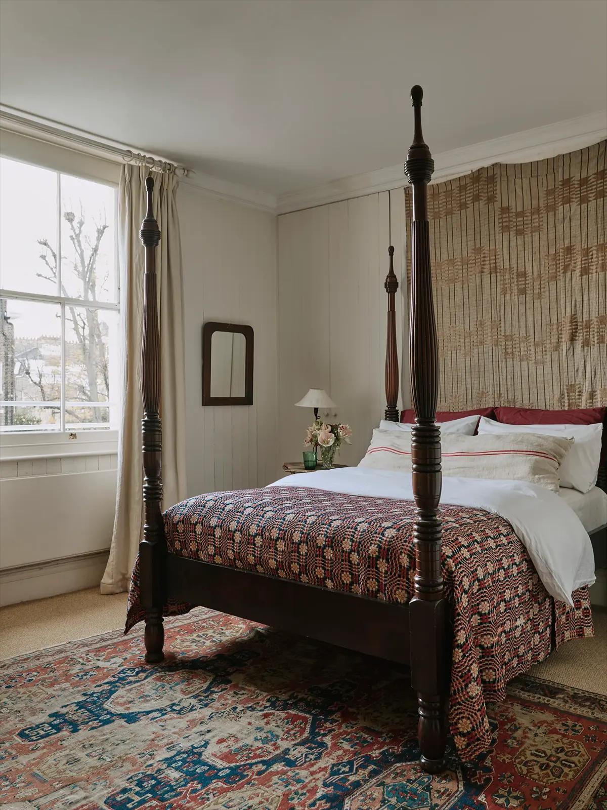 Спальня с деревянной кроватью с четырьмя столбиками и зеркалом на стене