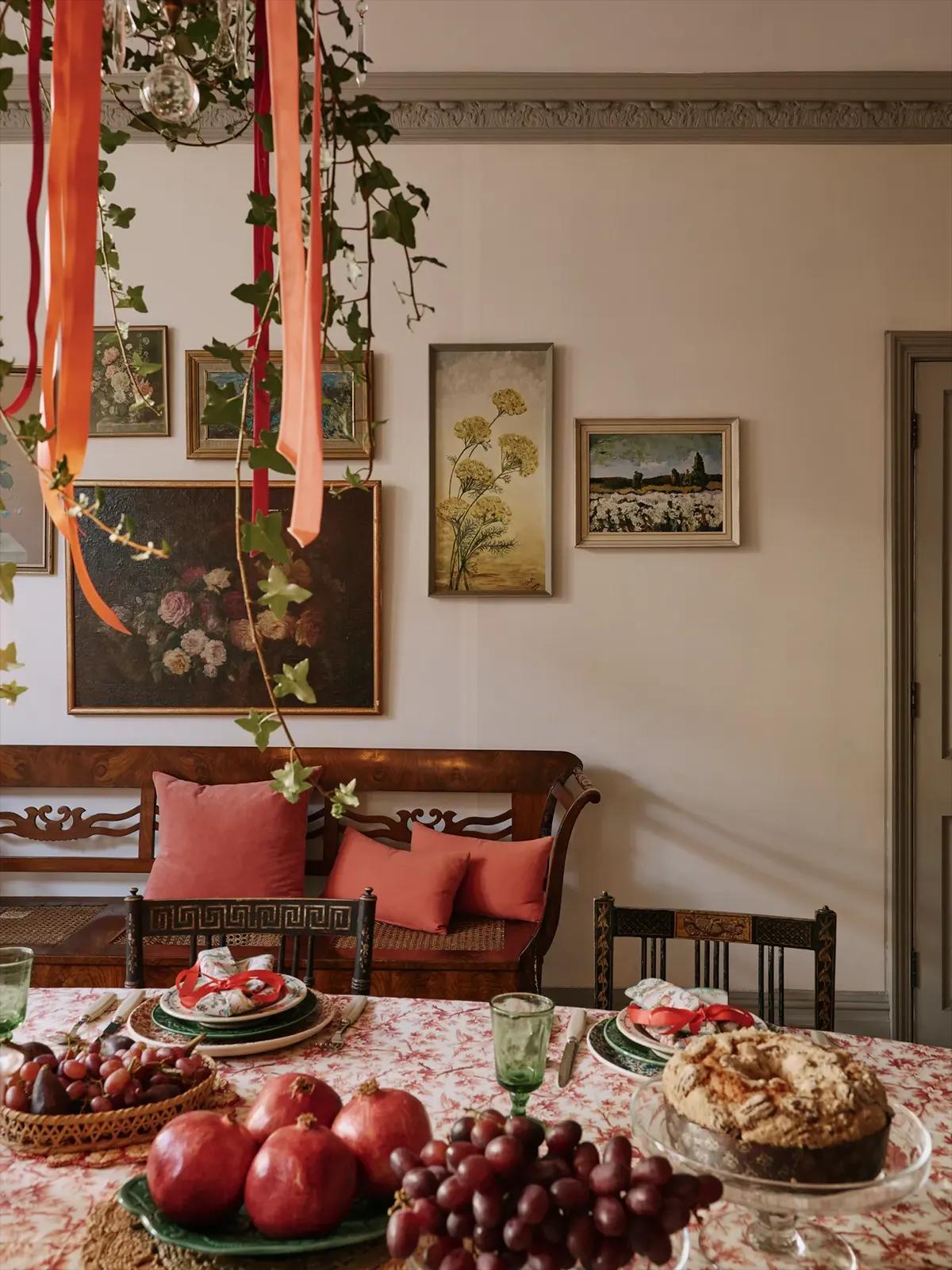 Стол с фруктами (гранаты, виноград), тортом, картинами на стене, плющом и оранжевыми лентами от люстры; деревянная скамейка с розовыми подушками