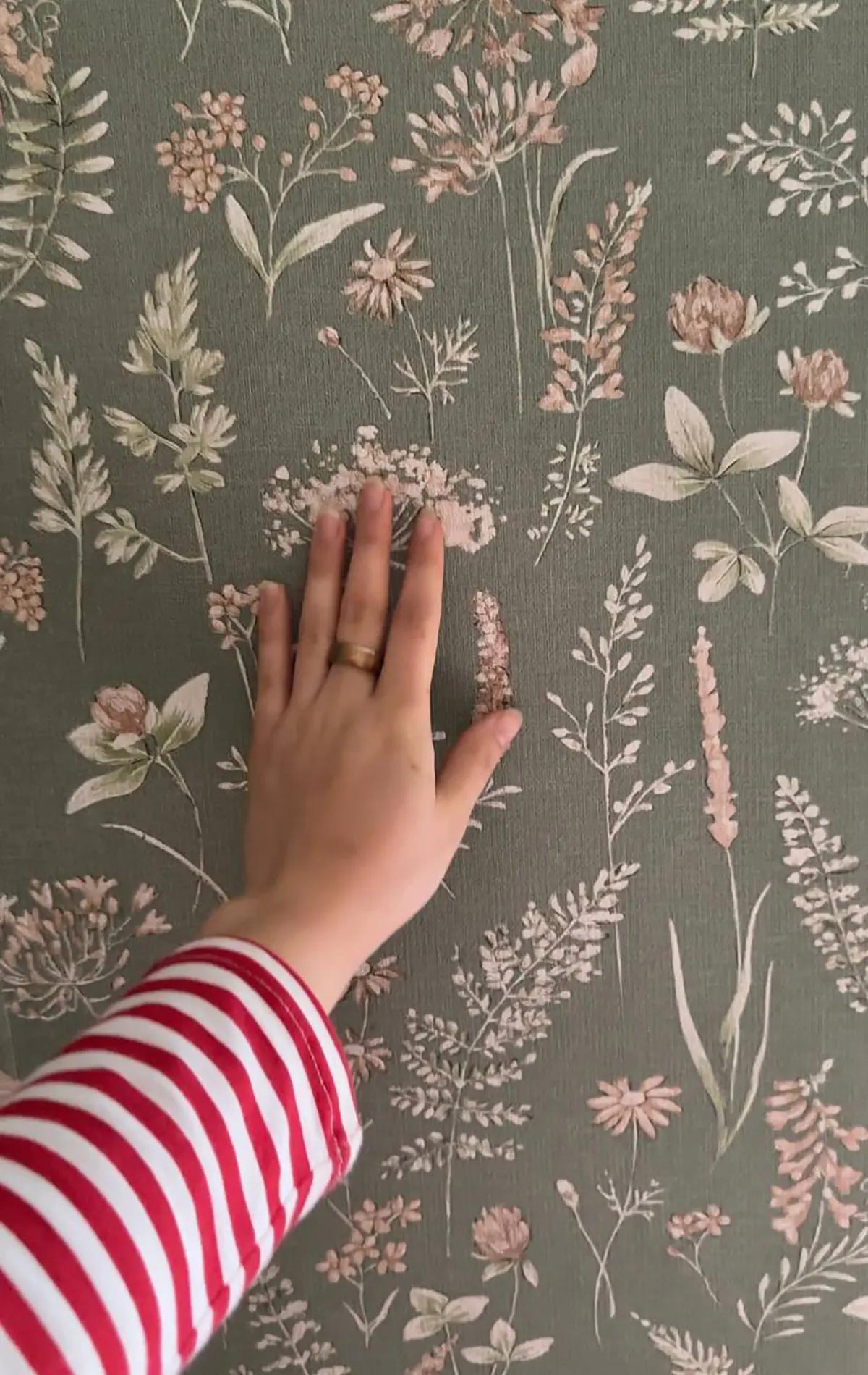 Рука на фоне зеленых обоев с растительным узором