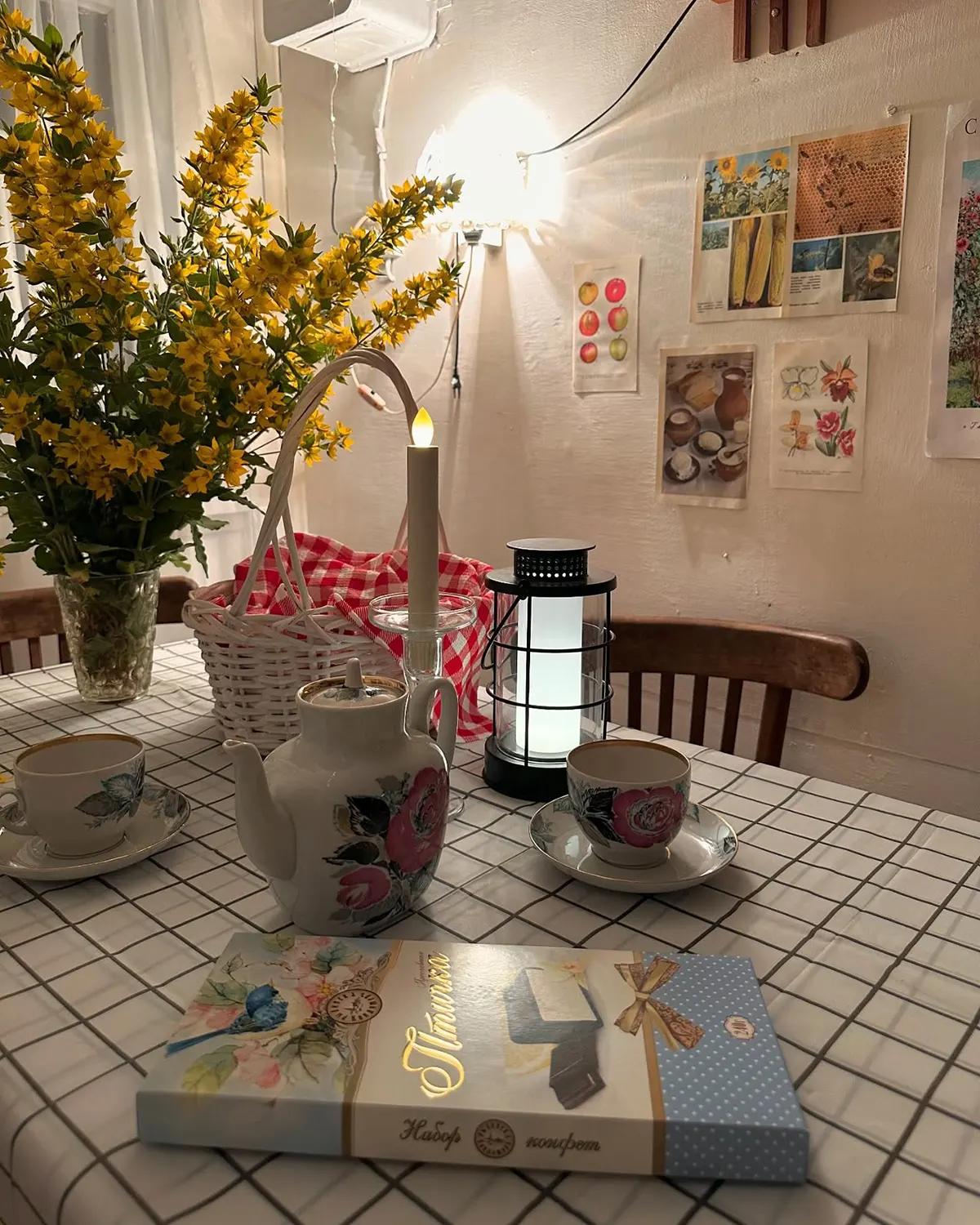 Уютная атмосфера на дачной веранде. Приглушенный свет, чайный сервиз на столе, желтые цветы в вазе, коробка конфет