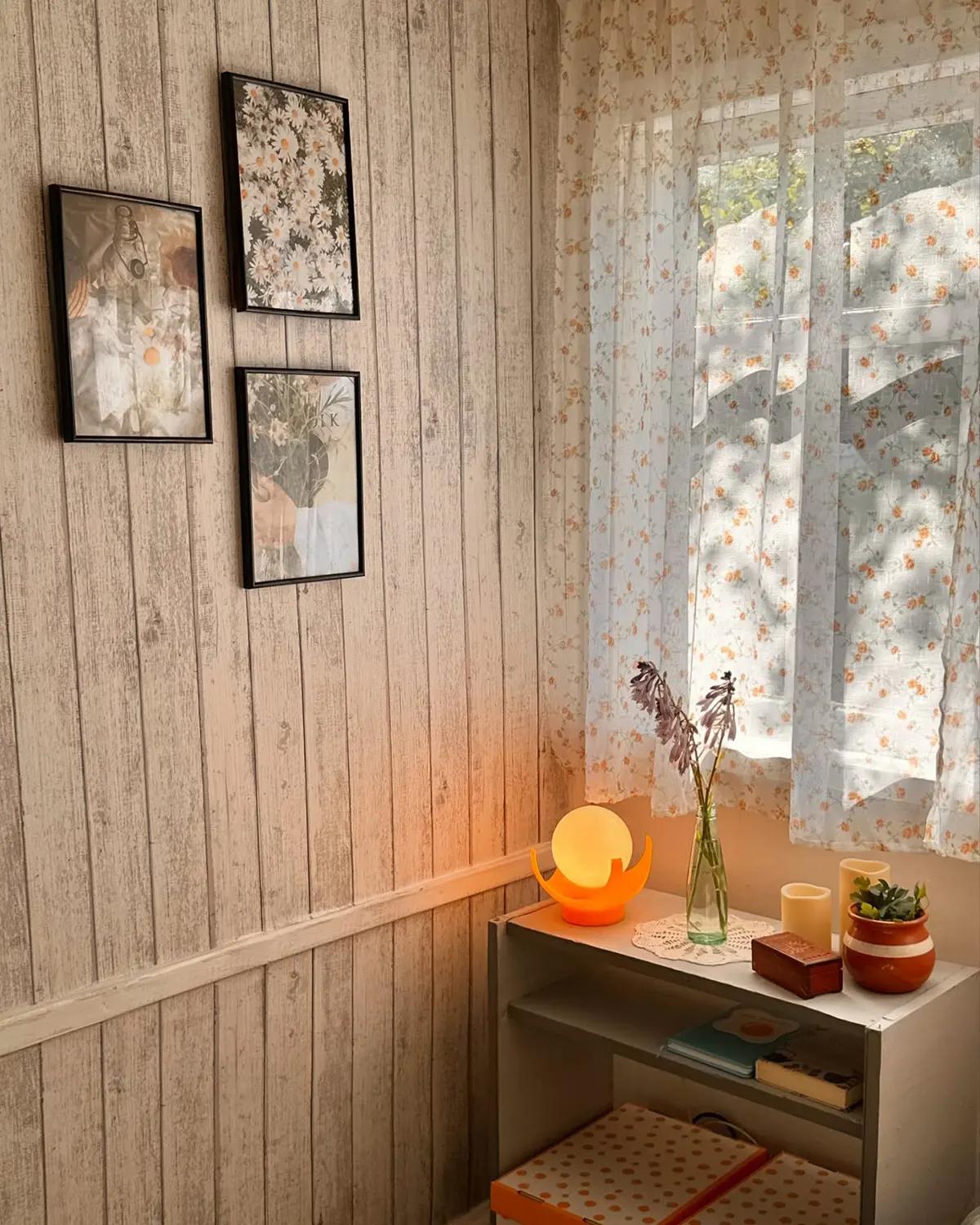 Уютный уголок в спальне в теплых тонах. На столе стоит ночник в форме шара, ваза с цветами и две свечи. 