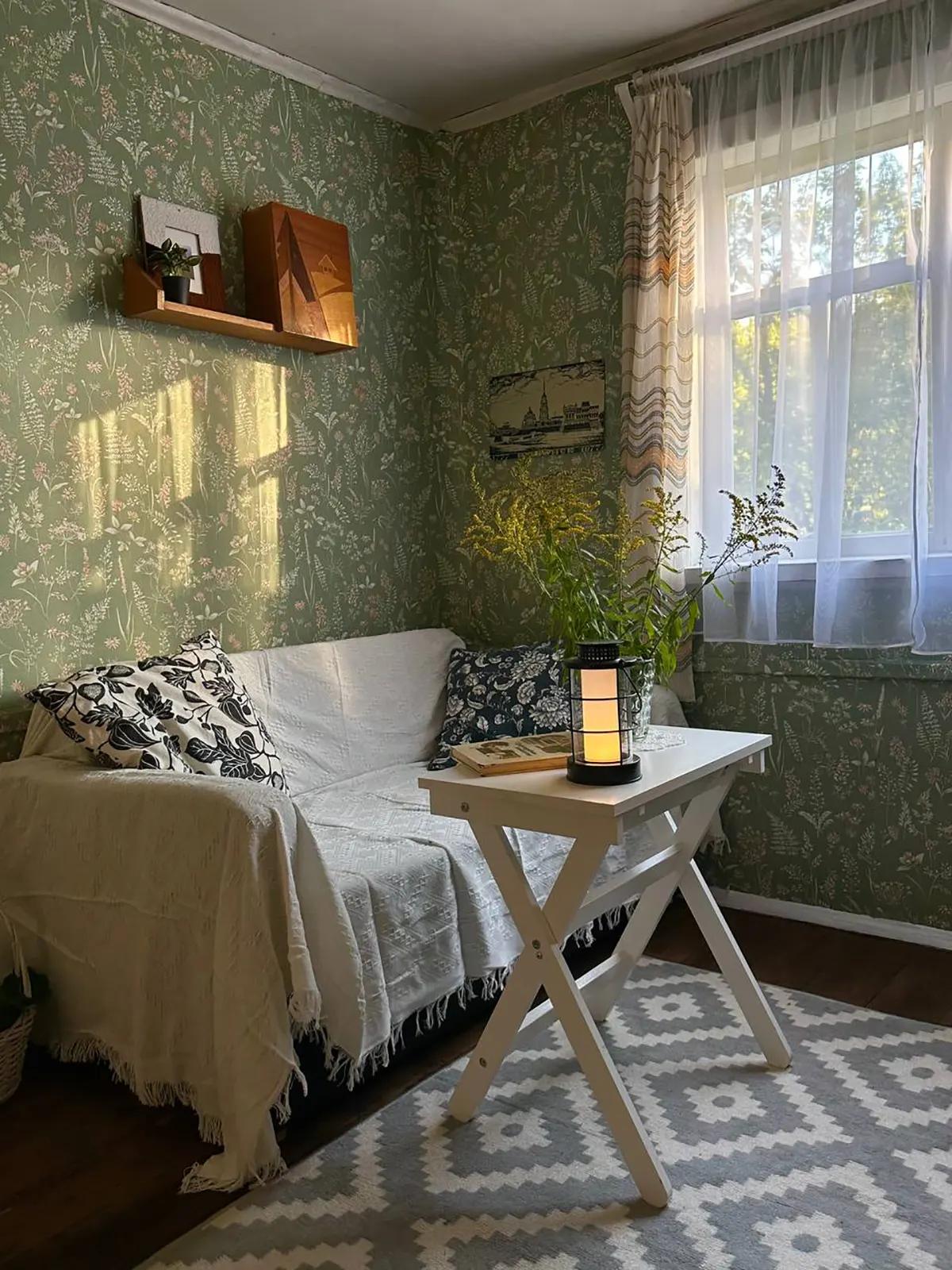 Уютный уголок гостиной, оформленный в деревенском стиле: диван с белым пледом, складной столик, занавески на окне