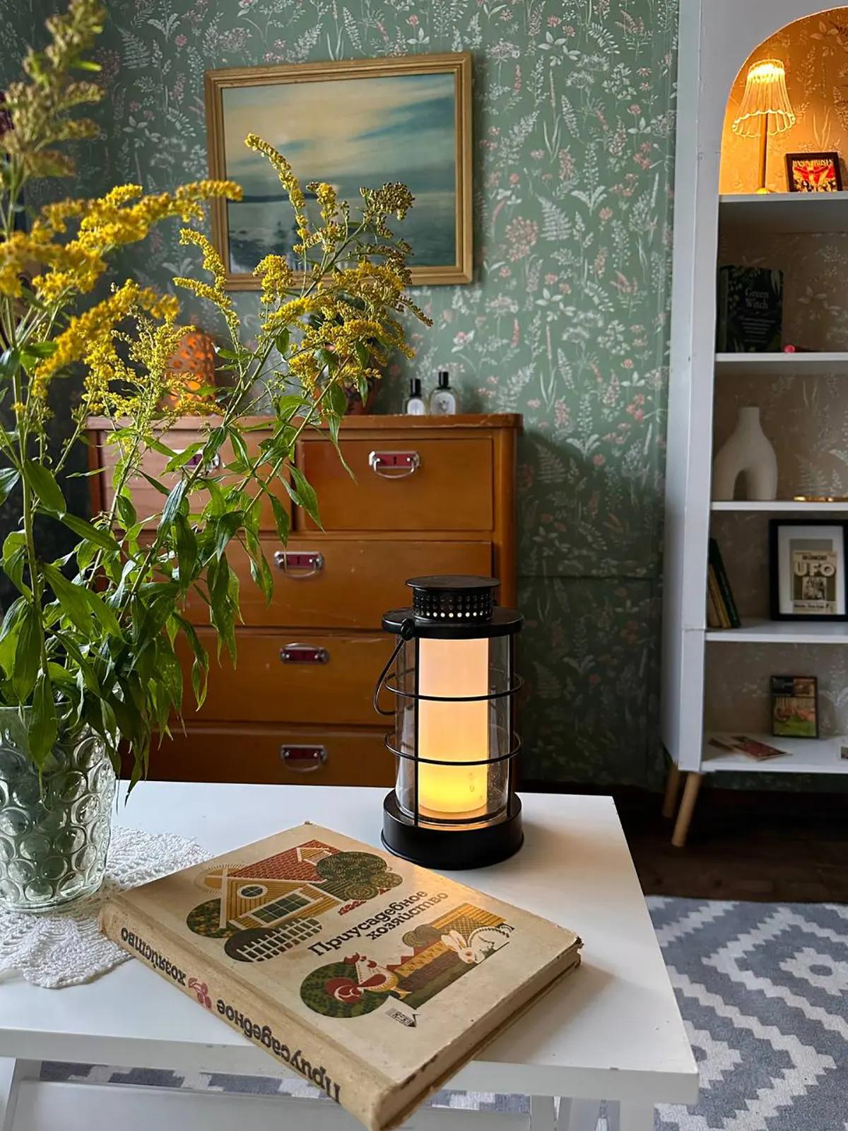 Книга, ваза с цветами и светодиодный фонарь STRÅLA от IKEA на белом журнальном столике в гостиной