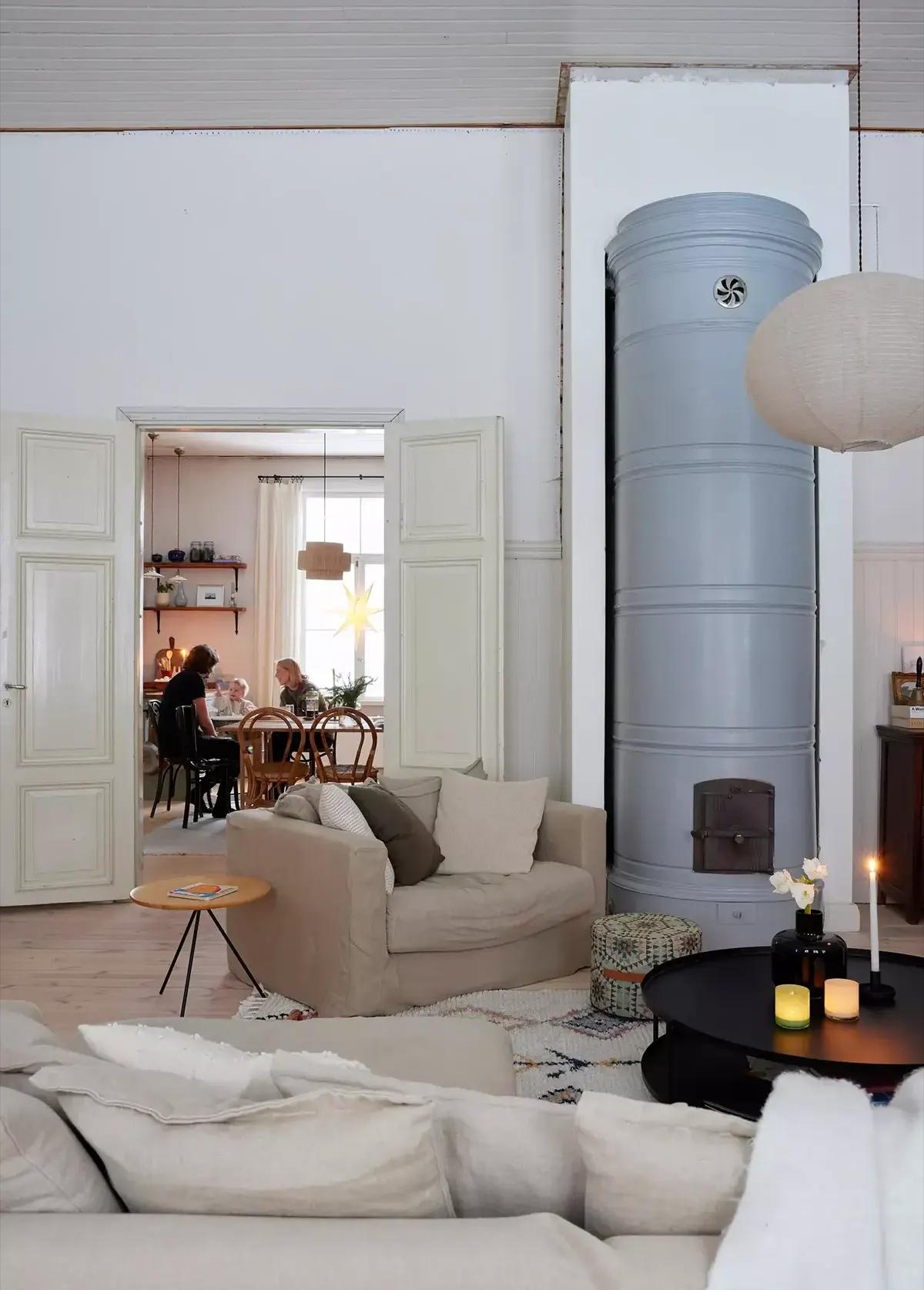 Гостиная с бежевым диваном, высокой серой печкой и видом на столовую зону