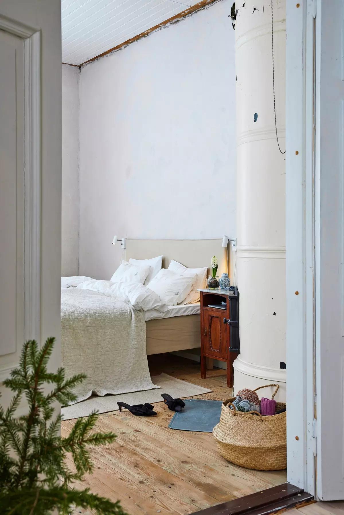 Спальня с кроватью, винтажной тумбочкой, белой печкой, корзиной с пряжей, туфлями и маленькой елочкой