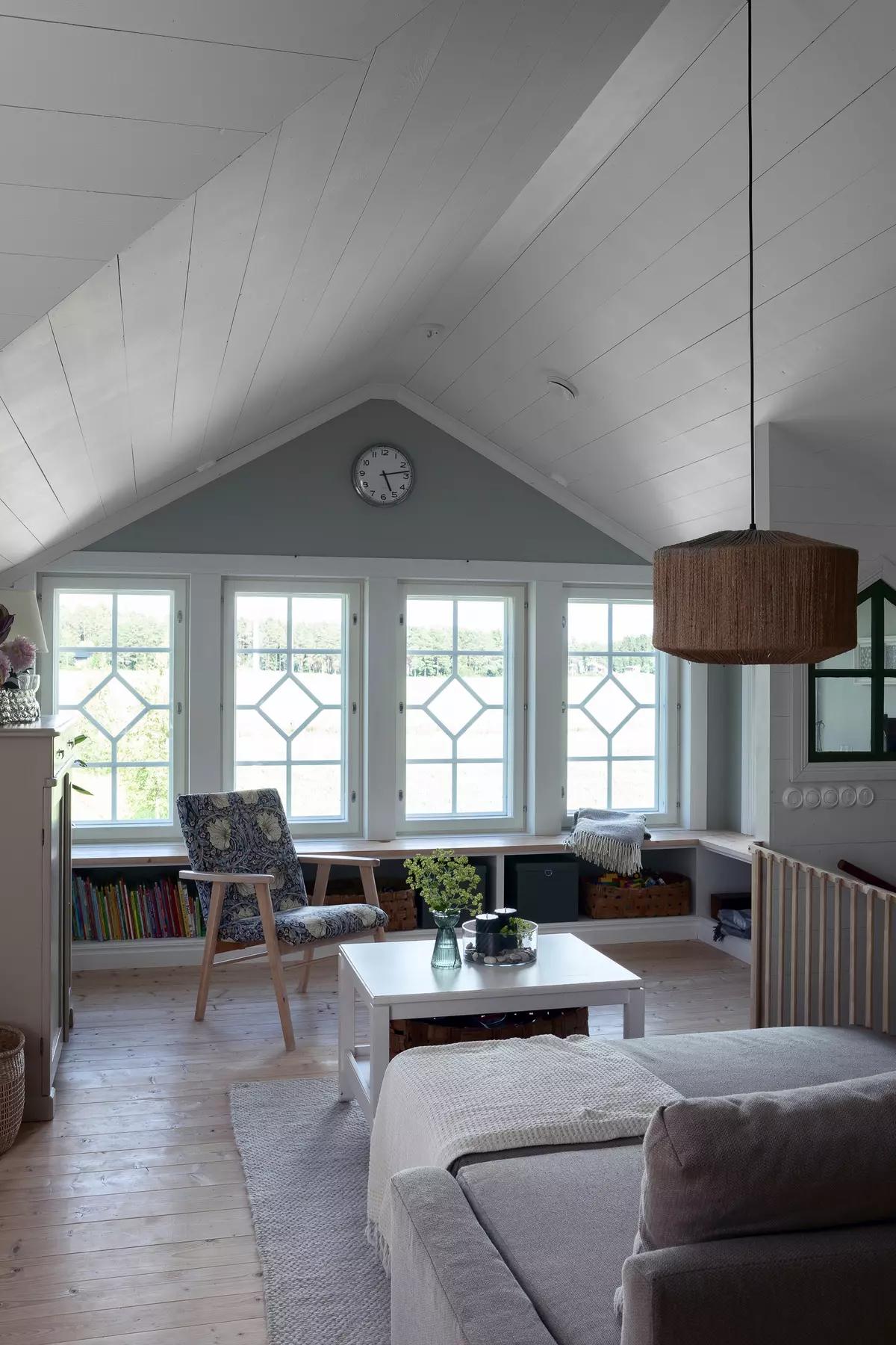 Мансардная комната с наклонным потолком, ретро-креслом, журнальным столом, диваном и большими окнами