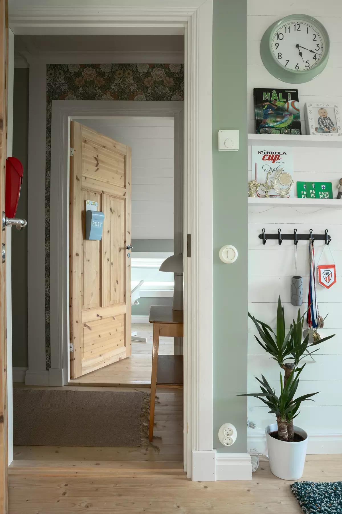 Открытая деревянная дверь в комнату. Стена с часами, полкой с книгами и вешалкой.