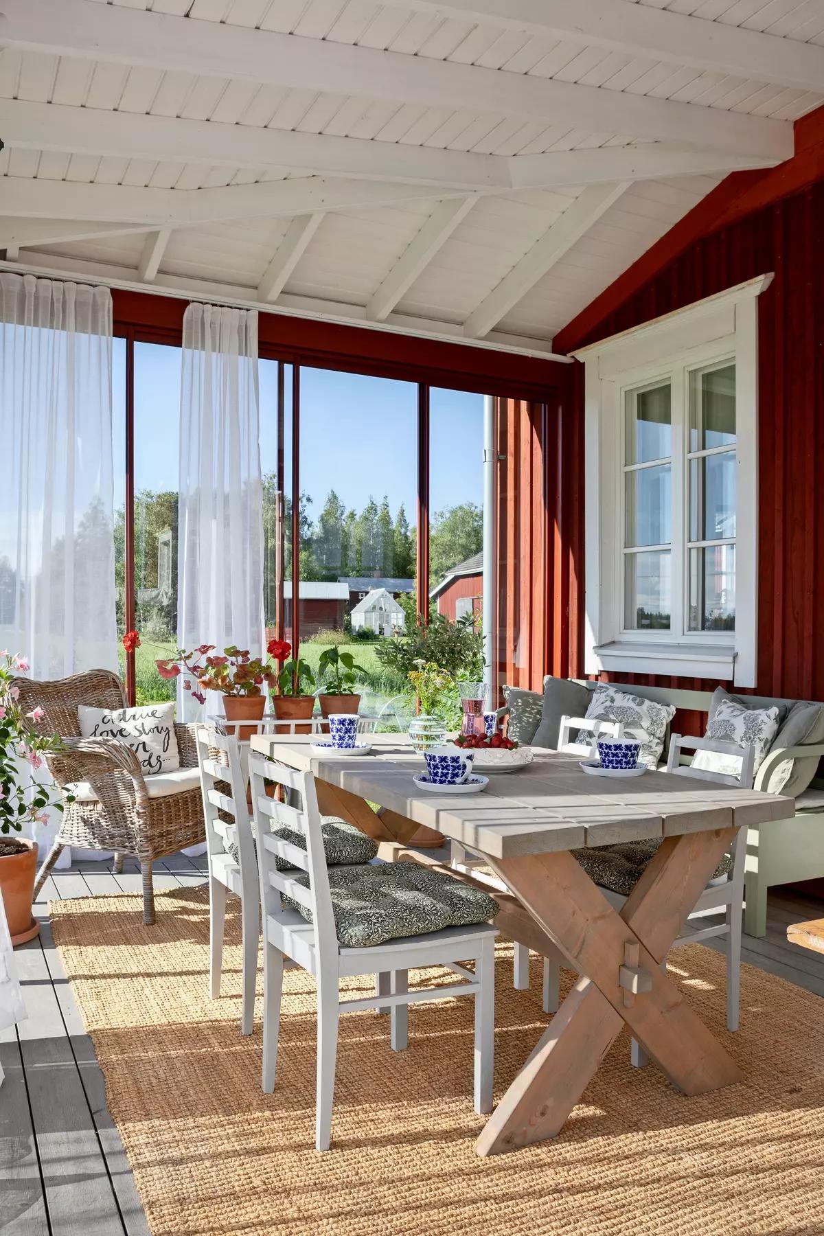Веранда с деревянным столом, белыми стульями, подушками, синими чашками и видом на природу