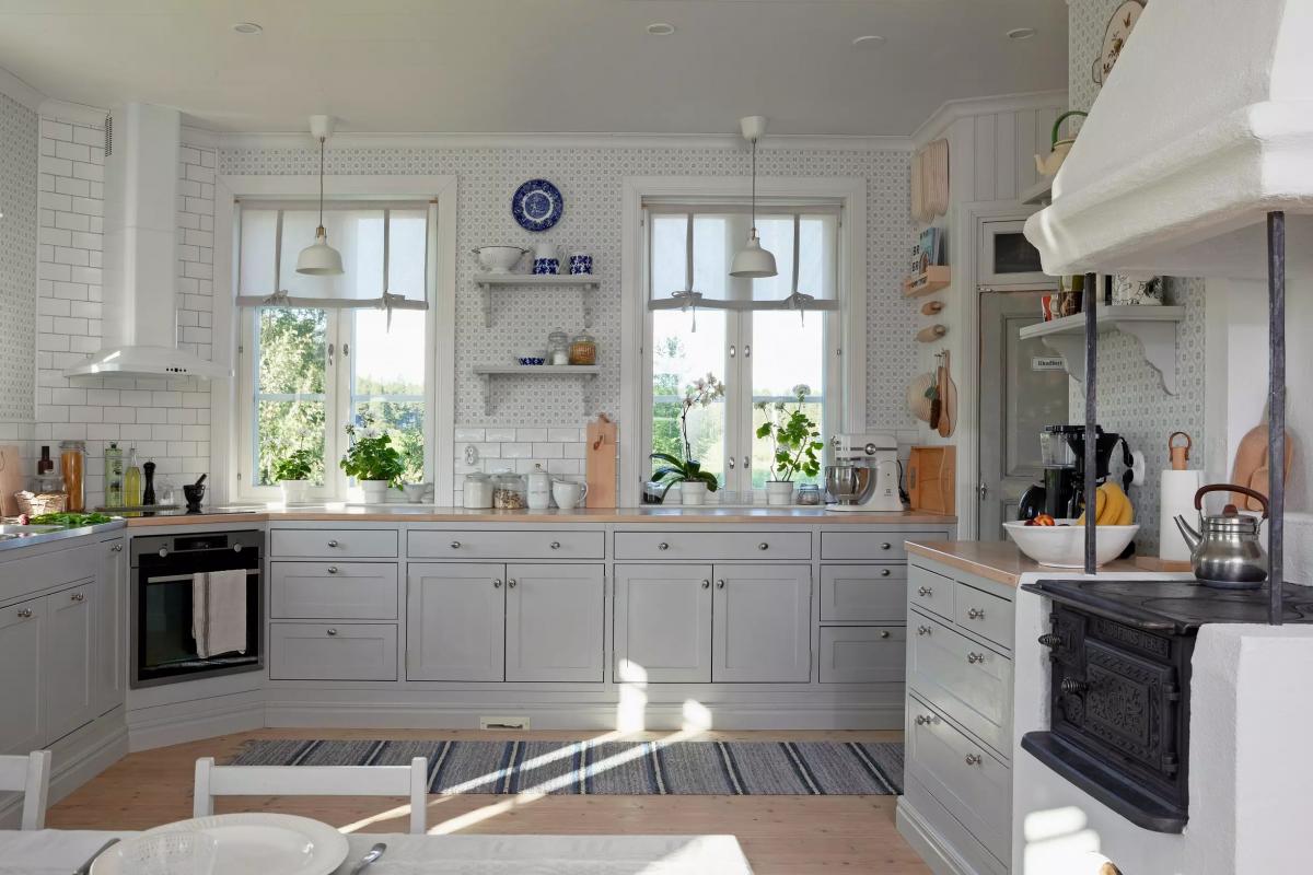 Светлая кухня с серыми шкафами, окнами, растениями, печью и духовкой