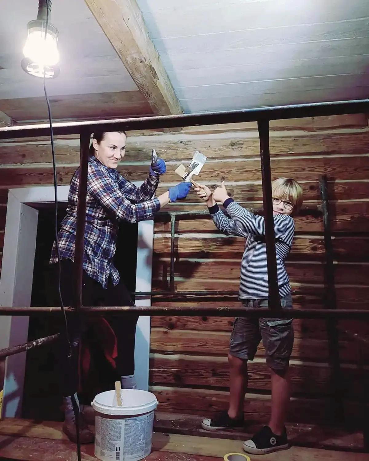 Женщина и мальчик красят потолок в деревянном доме