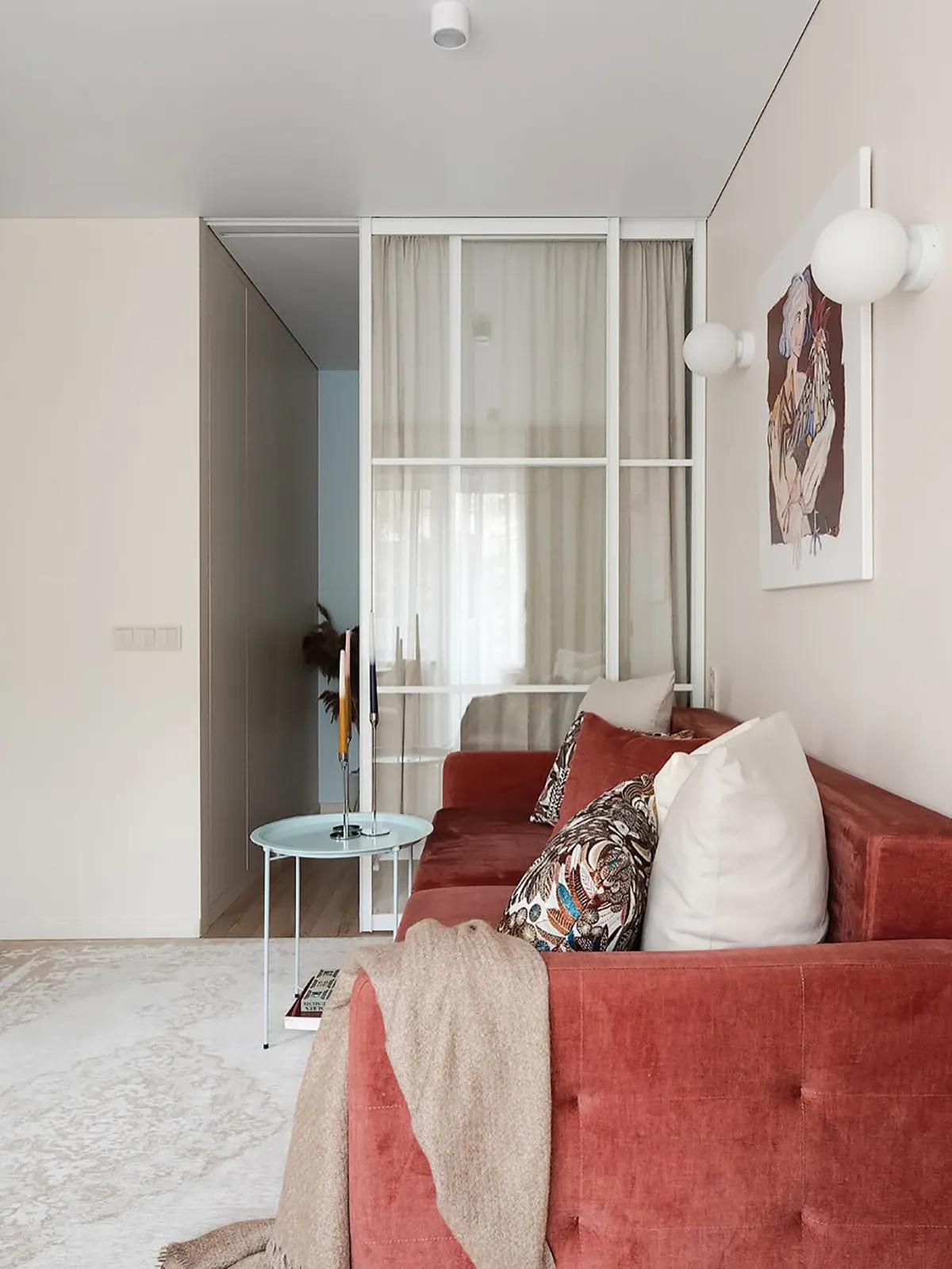 Гостиная с красным диваном, подушками, пледом, круглым столиком и картиной на стене