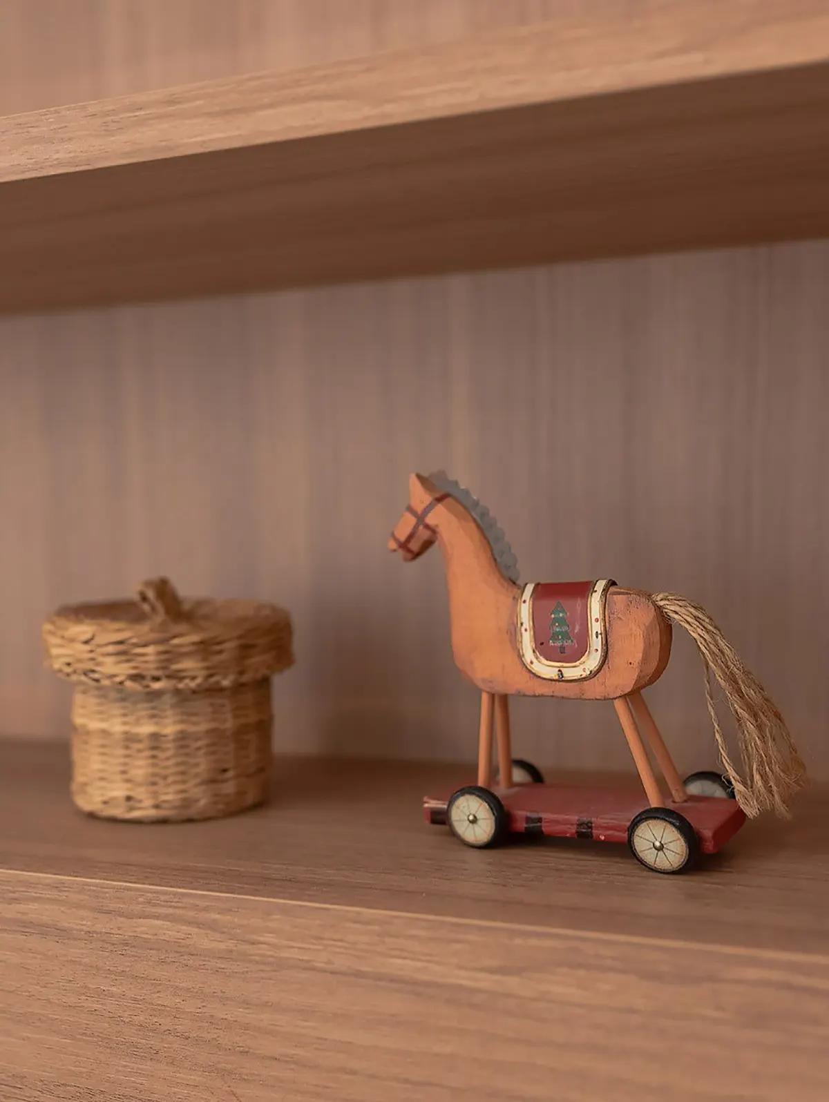 Крупный план деревянной полки с плетеной корзинкой и деревянной лошадкой на колесах