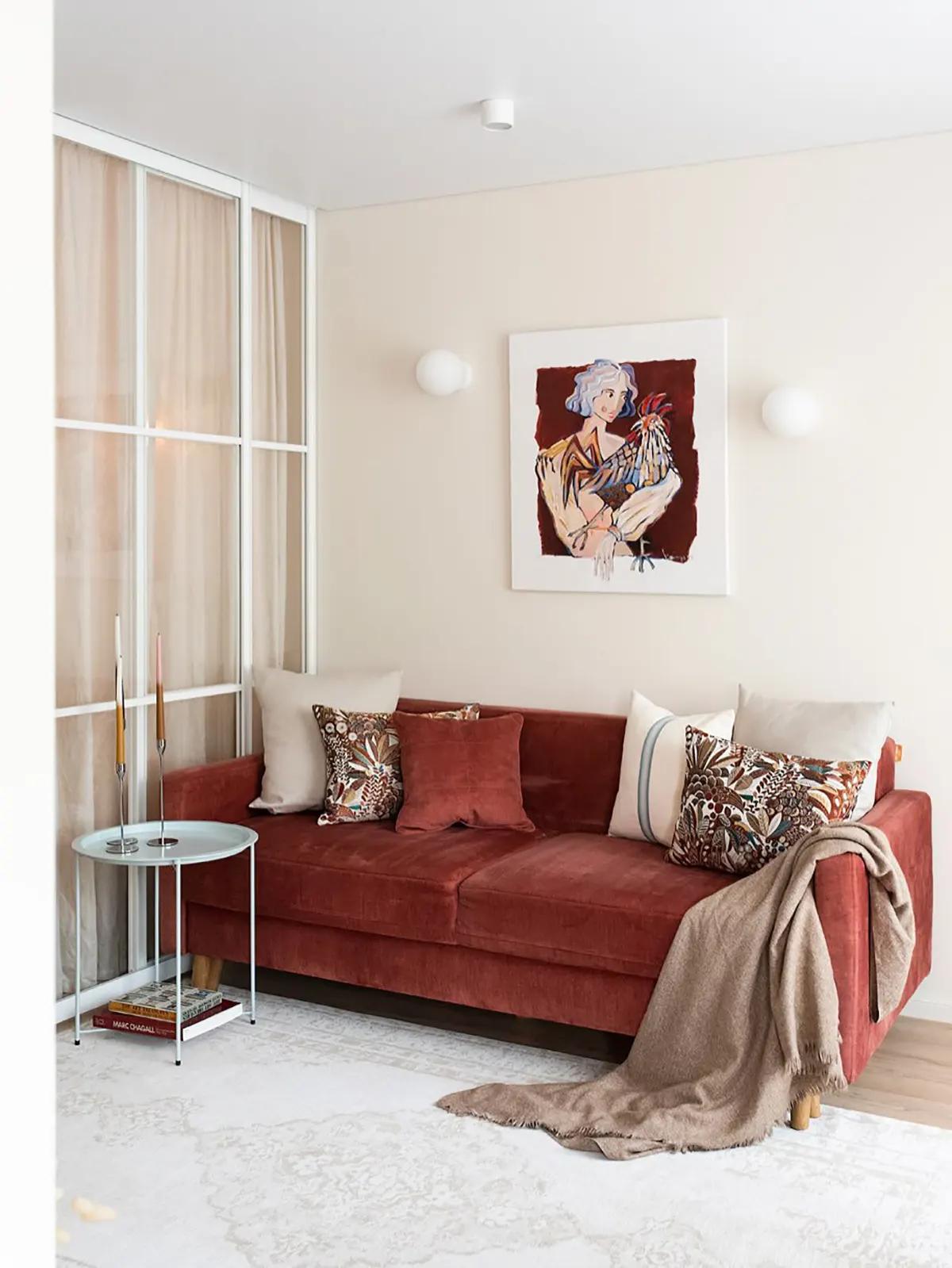 Красный диван с декоративными подушками и пледом в гостиной