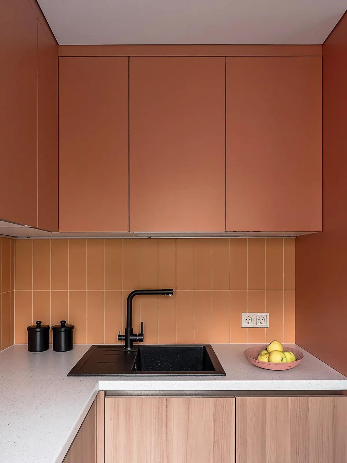 Терракотовая кухня с оранжевым фартуком, черной раковиной, банками и тарелкой с яблоками