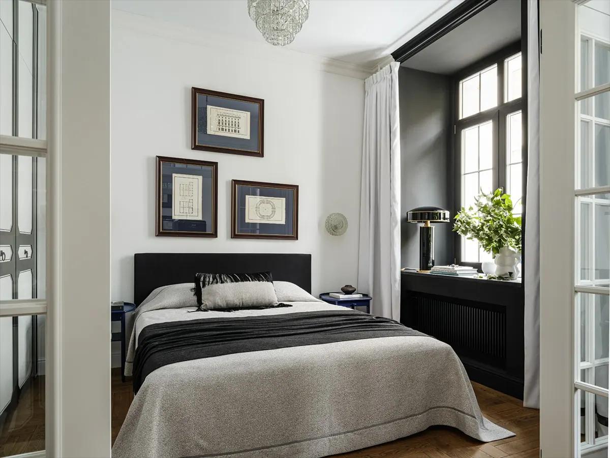 Вид через двери на спальню с кроватью, хрустальной люстрой и с постерами в рамках на стене