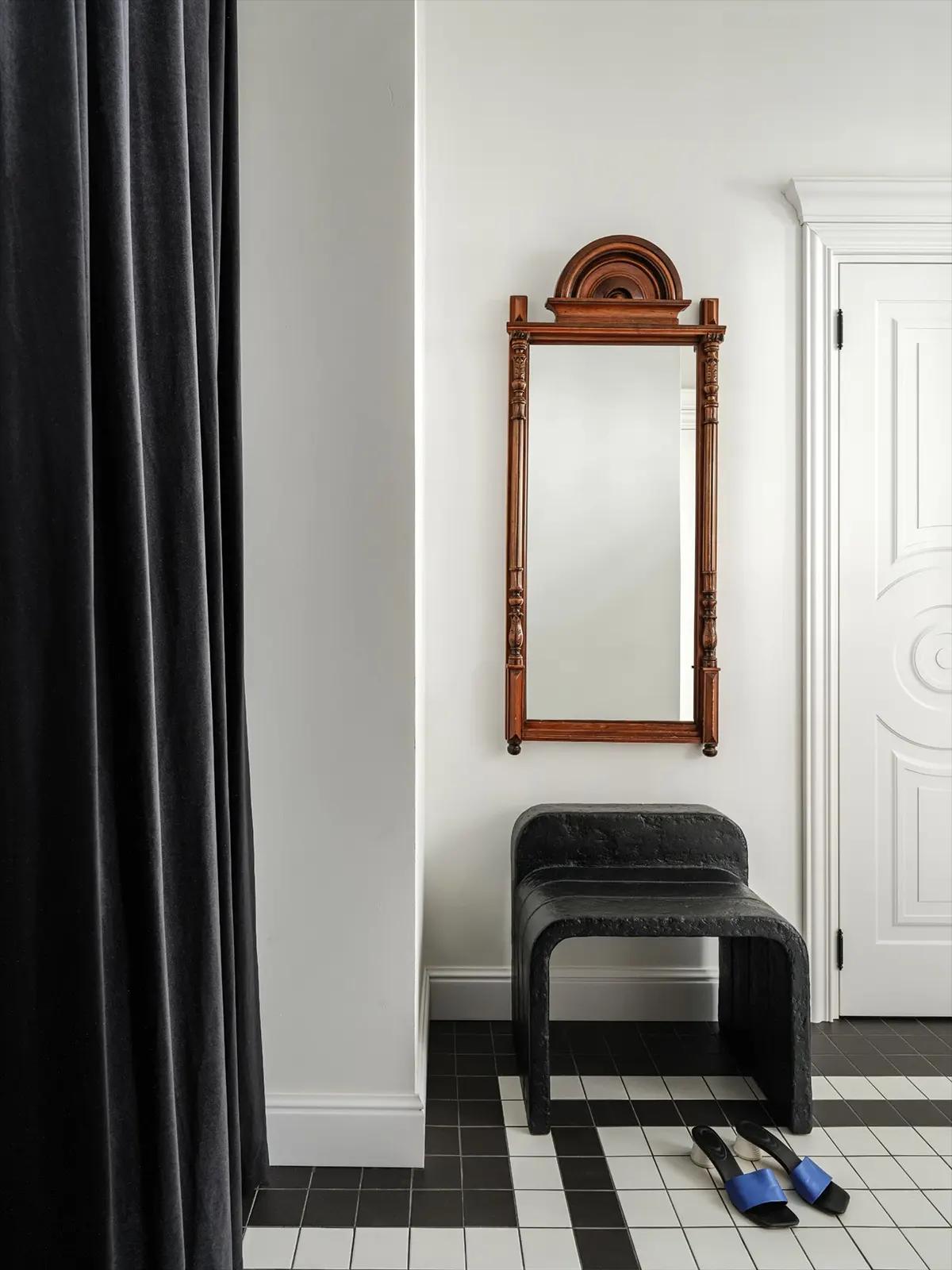 Прихожая с антикварным зеркалом в деревянной раме, черным табуретом и темной шторой.