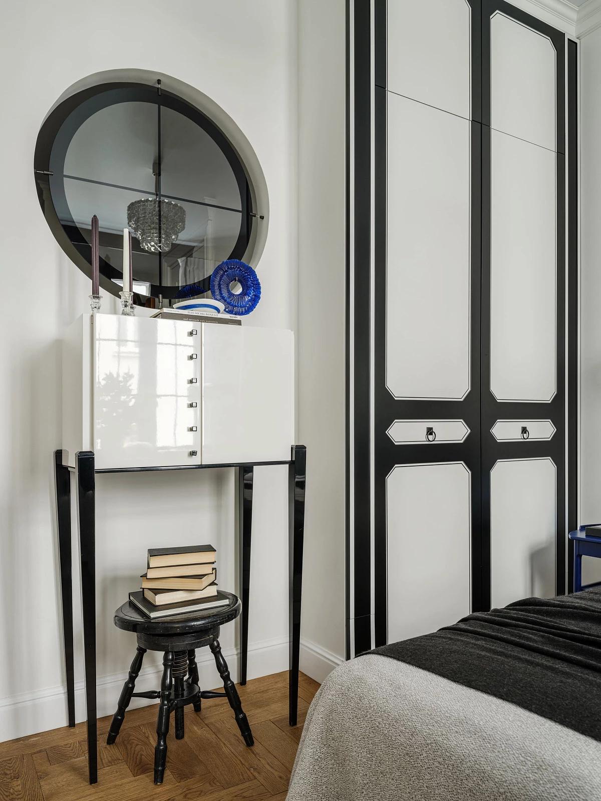 Белый шкафчик в спальне на длинных черных ножках. Стопка книг на антикварном черном табурете 