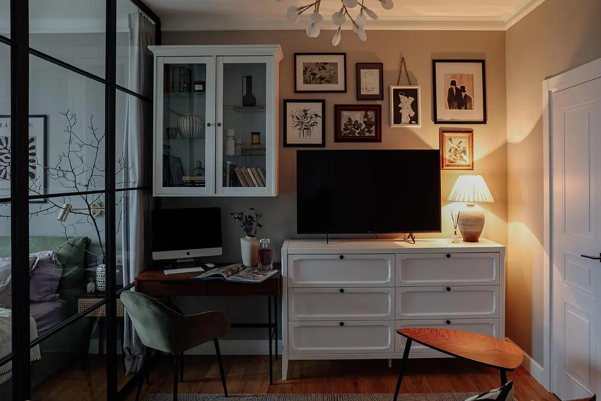 Уютная гостиная с белым комодом, телевизором, компьютером и лампой