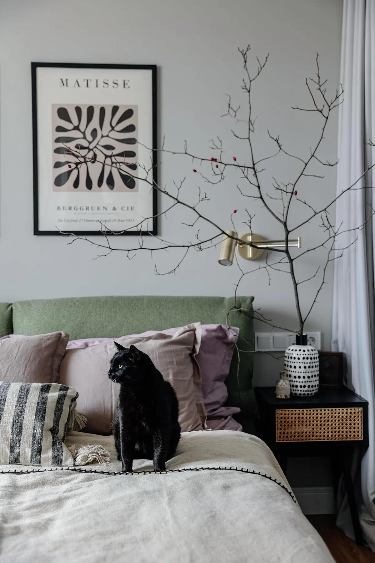 Спальня с зеленым изголовьем, черным котом на кровати и веткой в вазе