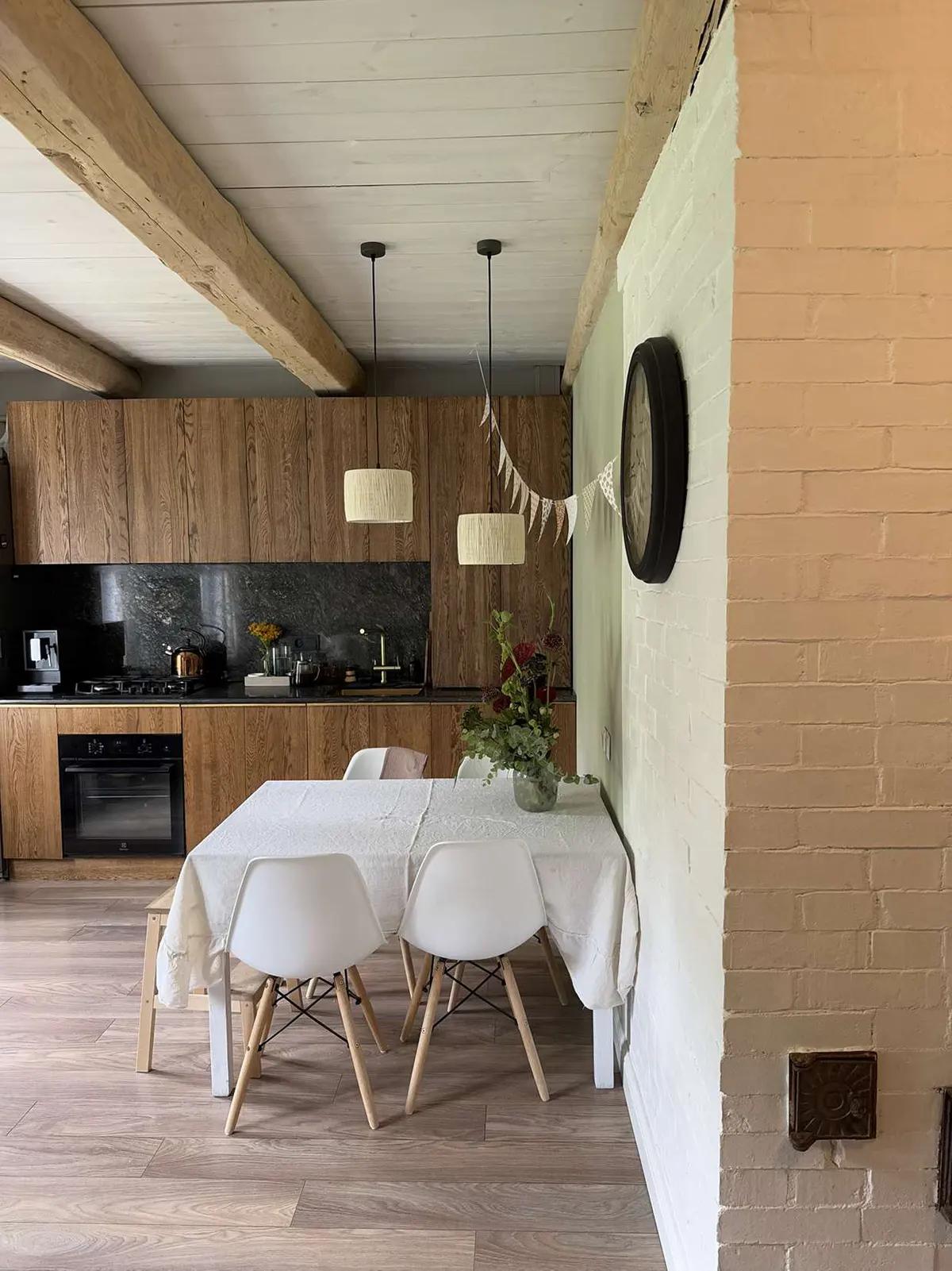 Кухня с деревянными шкафами, черной столешницей, белым столом, стульями, гирляндой из флажков и цветами