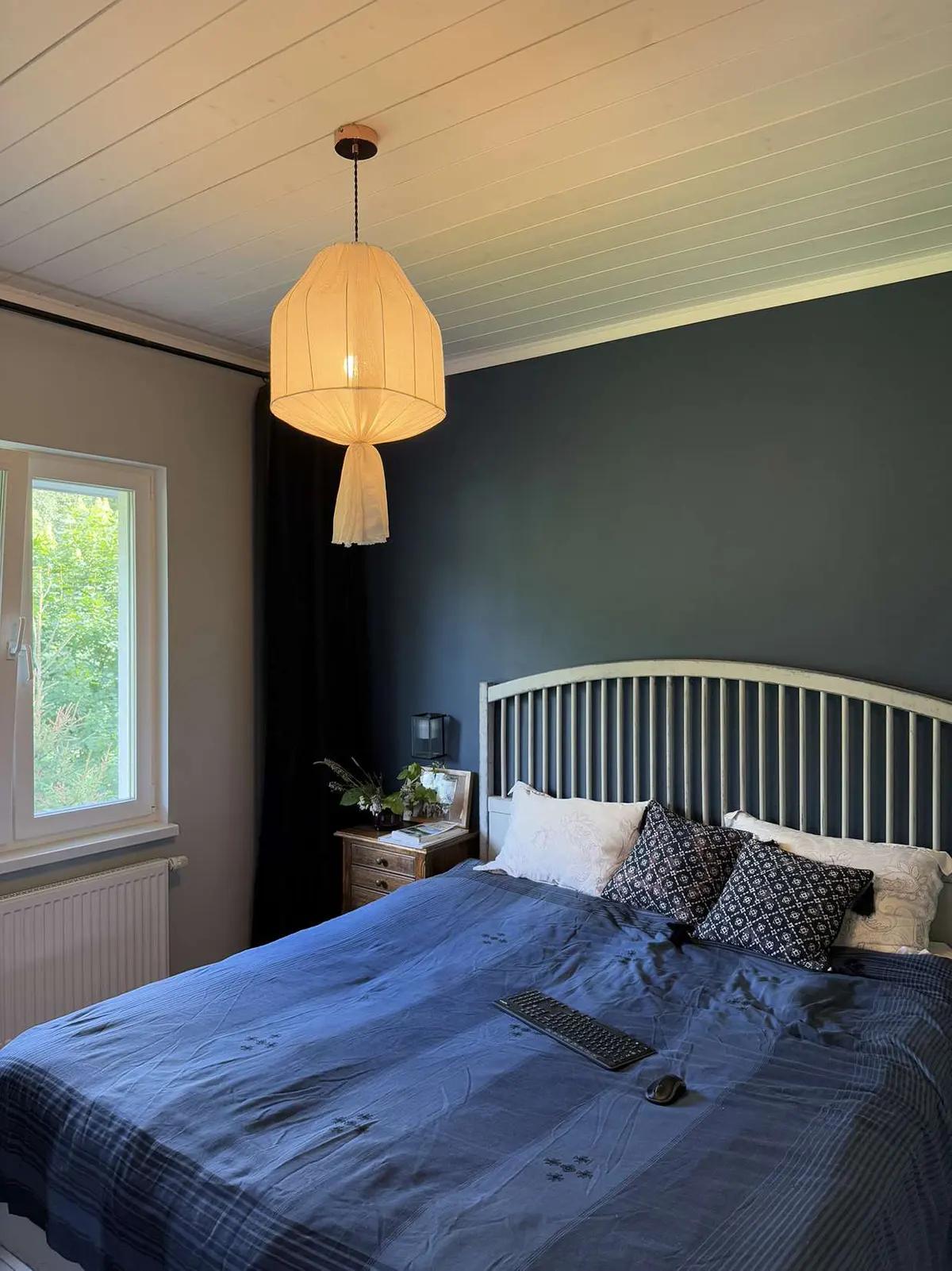 Спальня с подвесным светильником, окном, черной шторой, кроватью с синим постельным бельем