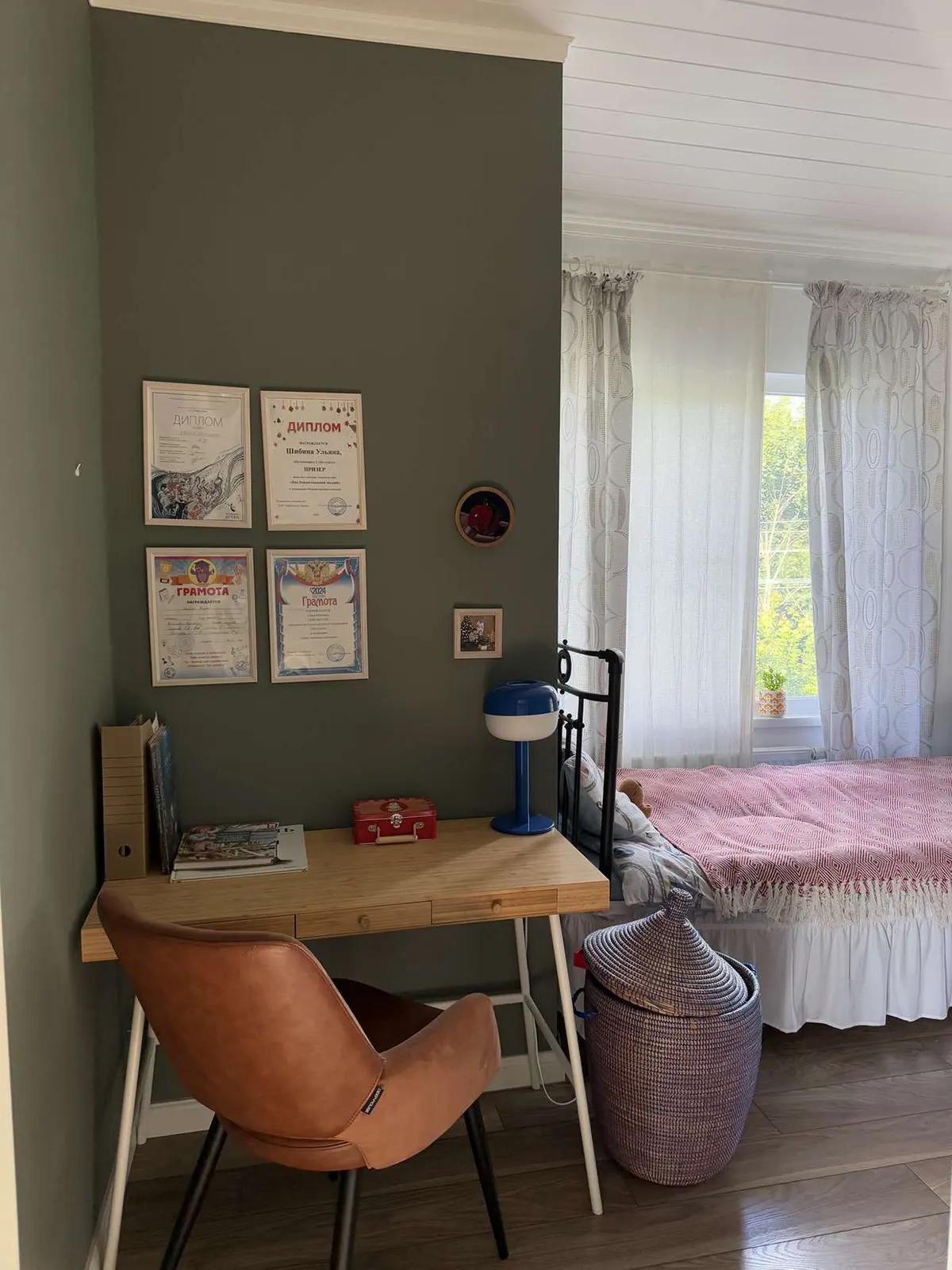 Угол комнаты с письменным столом, коричневым креслом, дипломами на стене