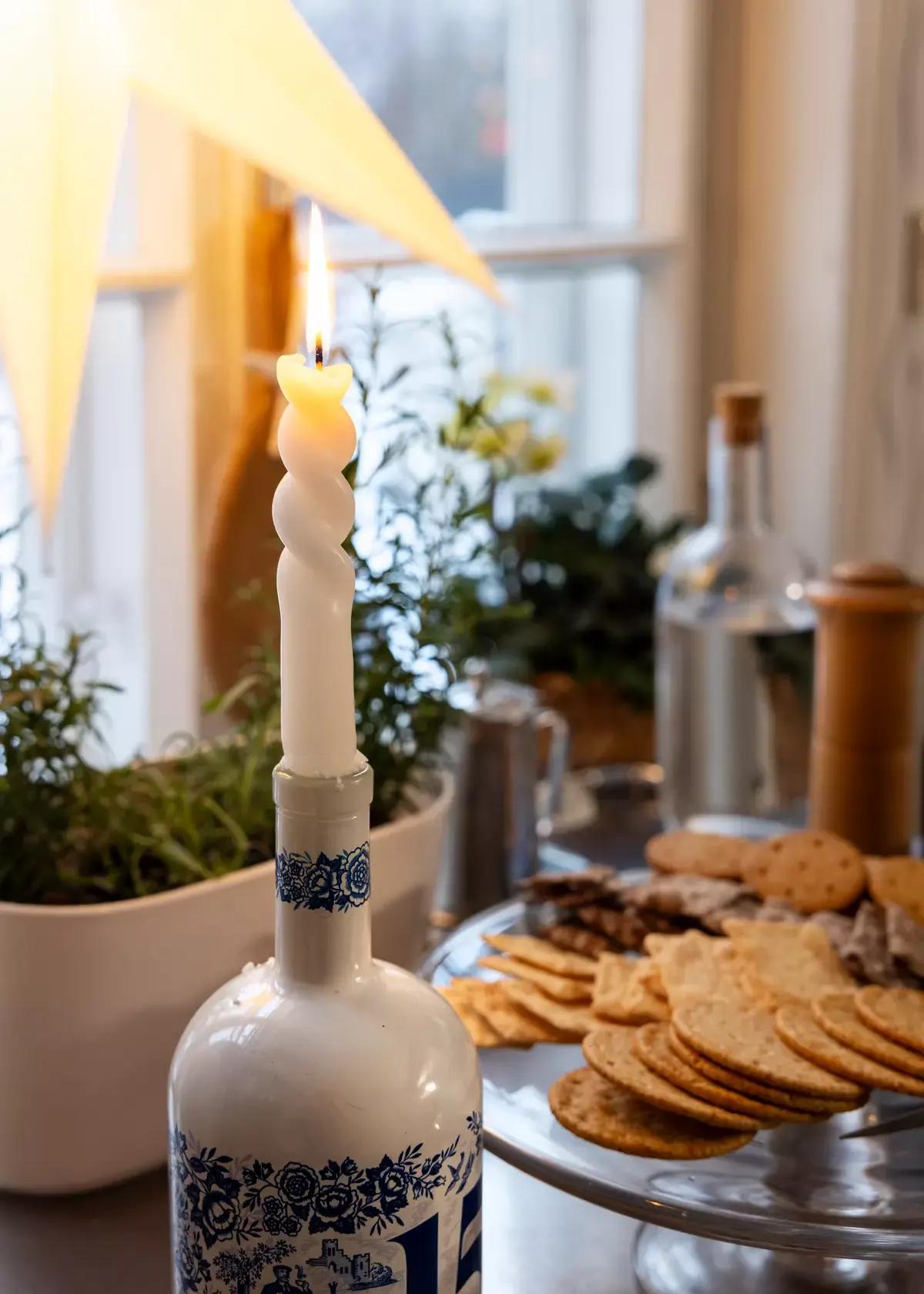 Горящая свеча витой формы на декоративной бутылке с синей росписью